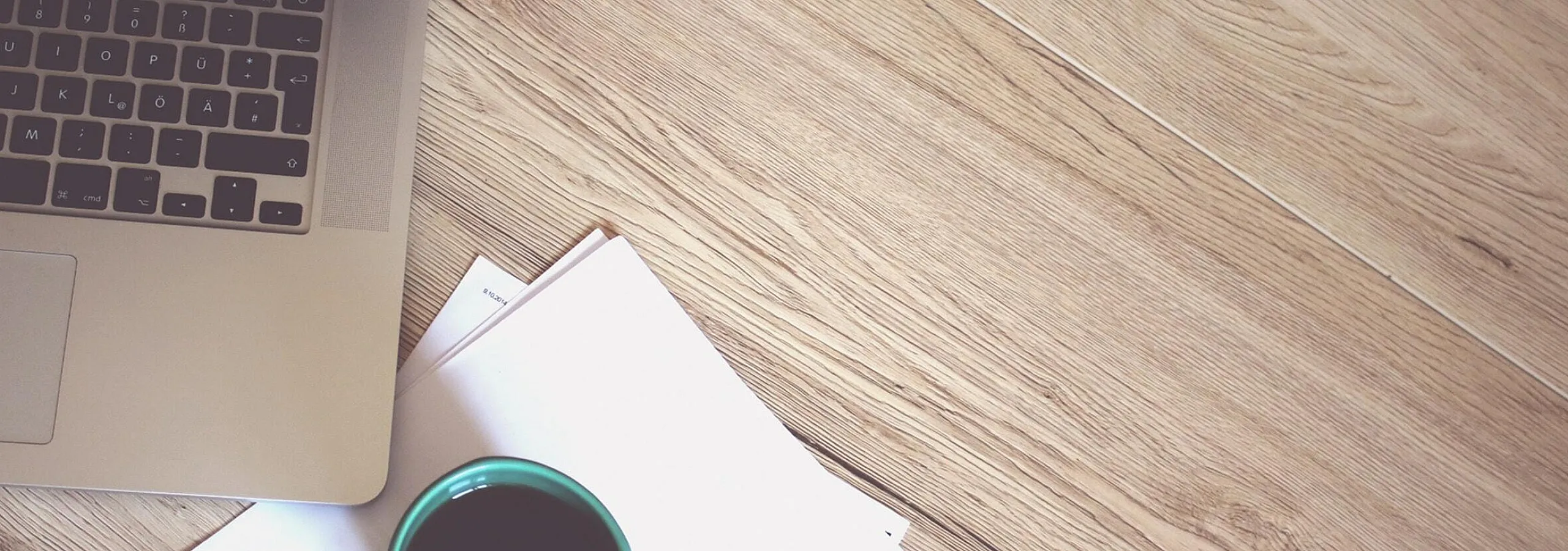 Cozy workspace with a laptop, steaming coffee in a turquoise cup, and documents on a stylish wooden floor.