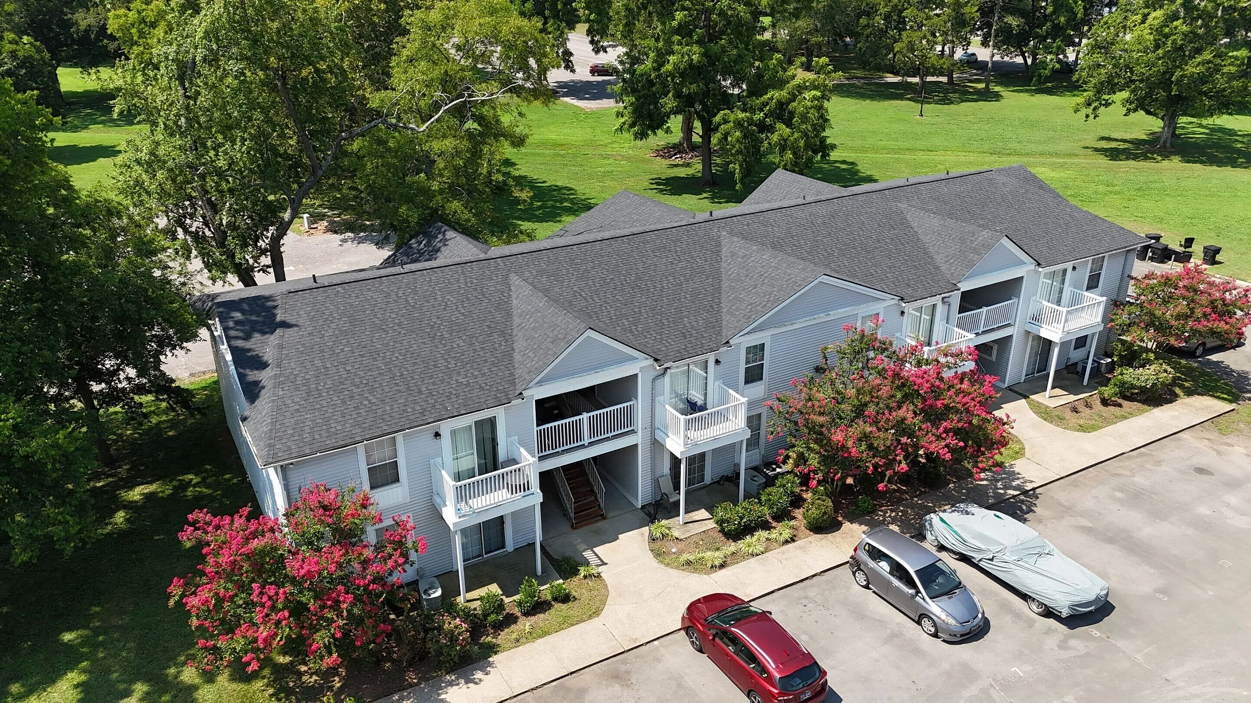Charming apartment building surrounded by lush greenery and vibrant flowering trees, featuring private balconies and convenient parking in a serene community setting.