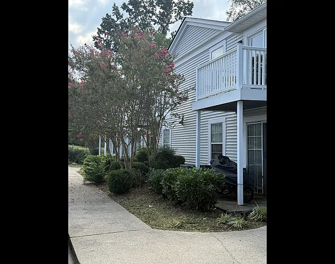 Charming exterior view of a modern apartment featuring a private balcony and vibrant landscaping with blooming trees.
