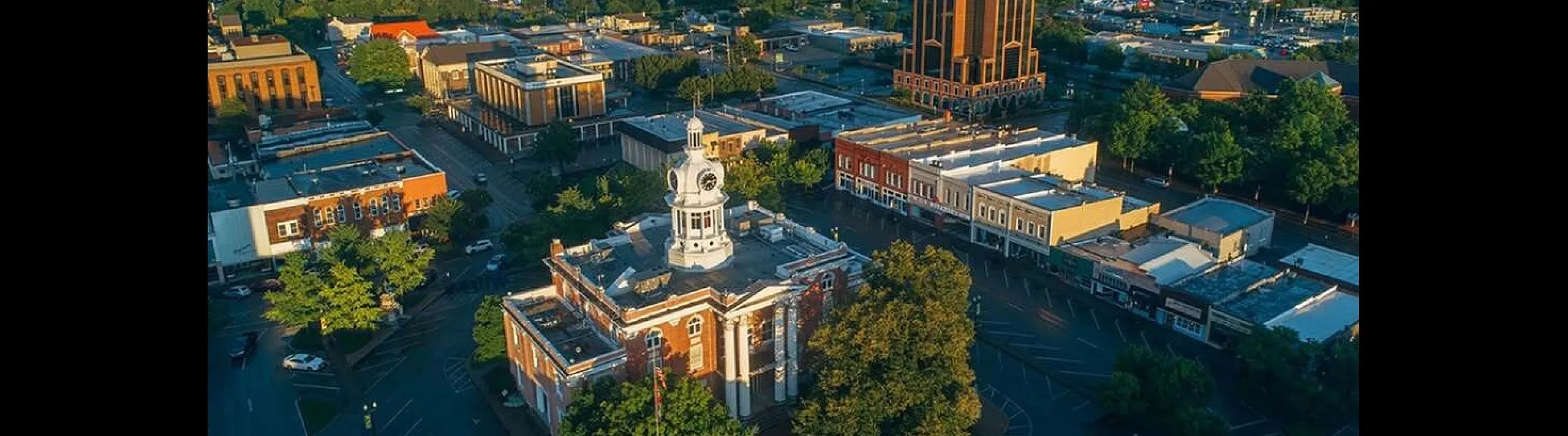 Charming aerial view of a picturesque cityscape featuring historic architecture, lush green trees, and a timeless clock tower at sunrise.