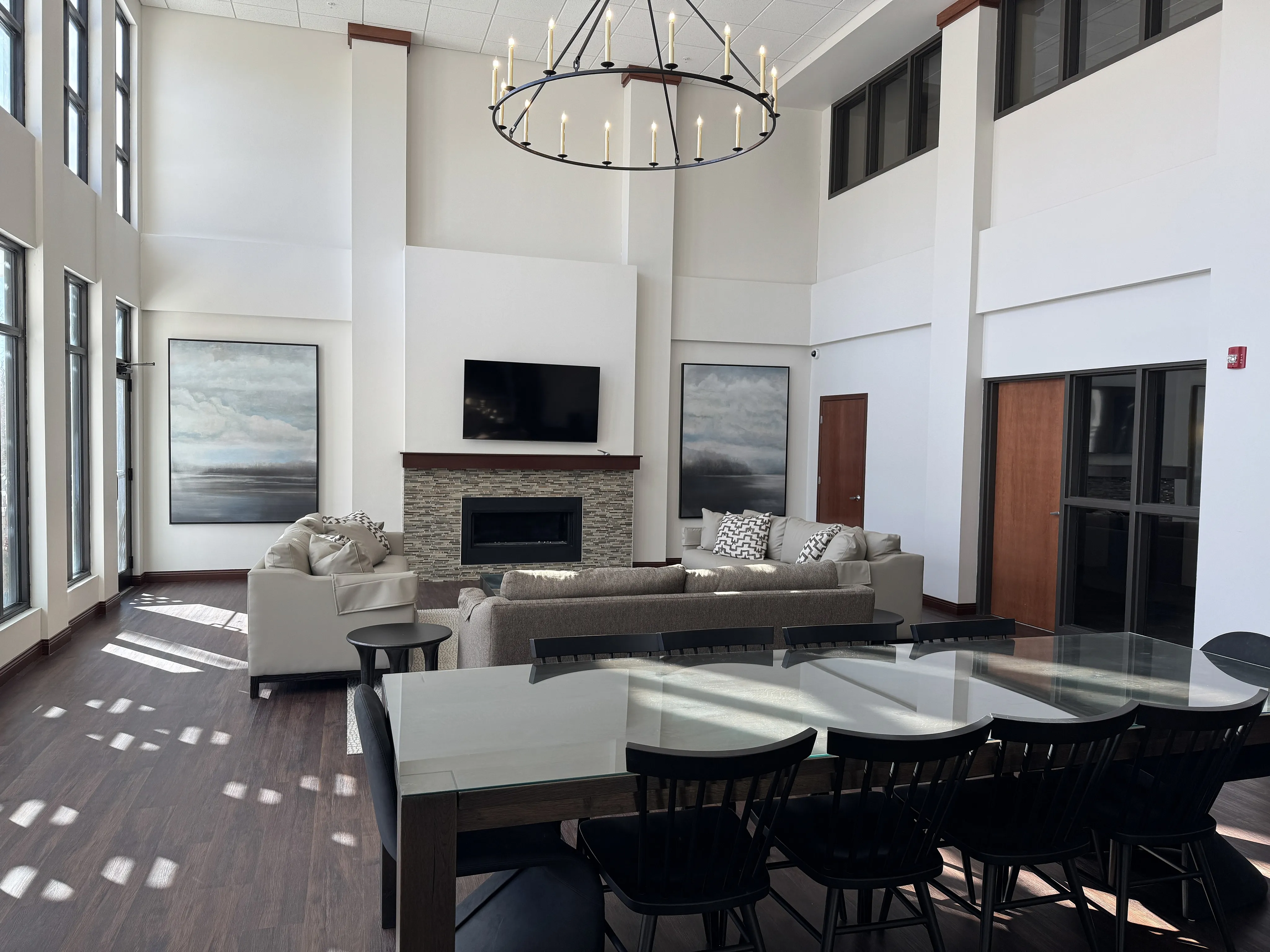 Spacious modern community room with high ceilings, elegant chandelier, and cozy fireplace, perfect for relaxation and entertaining.