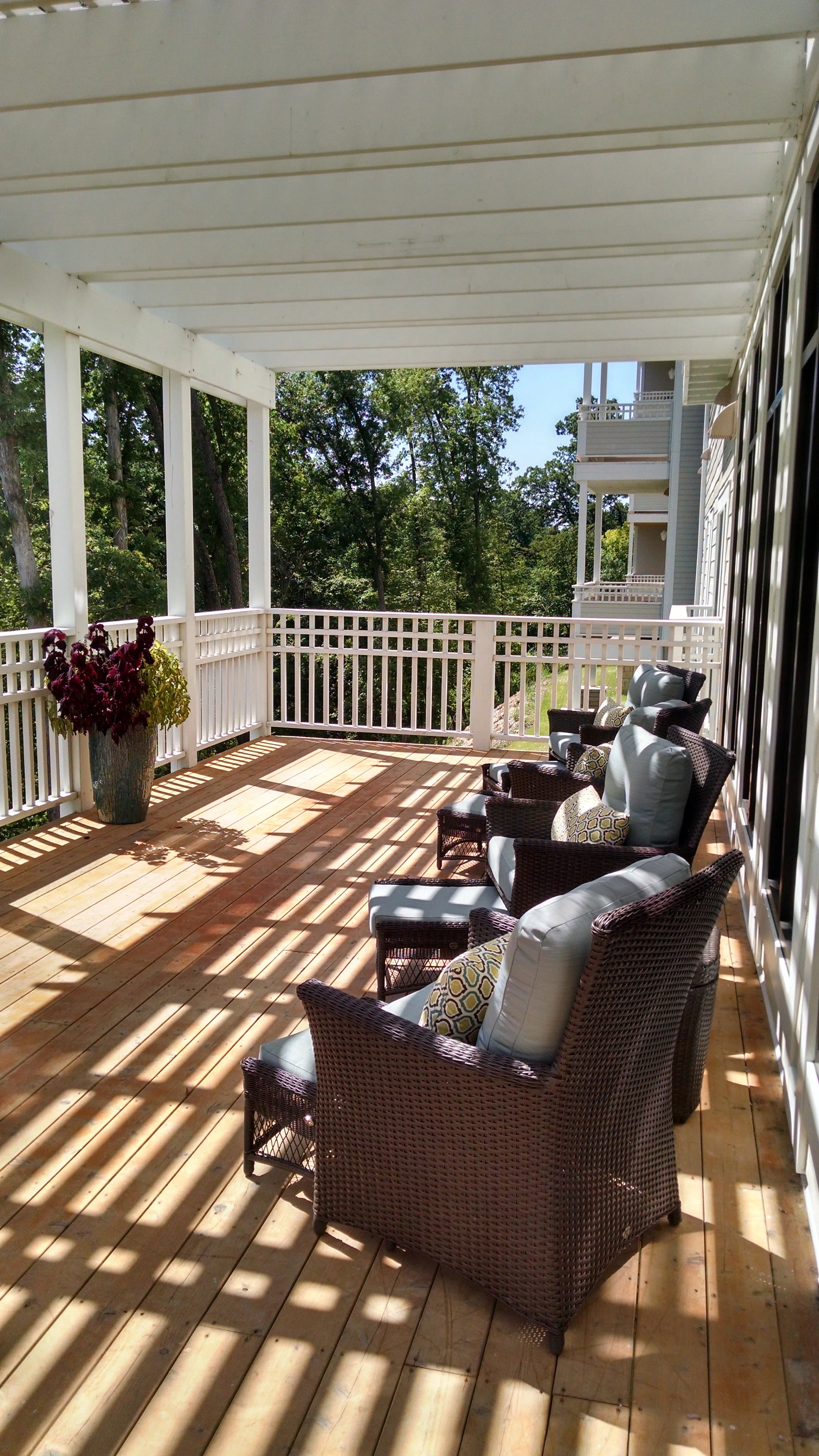 Charming sunlit community porch with cozy wicker chairs and vibrant potted plants, offering a serene outdoor space.