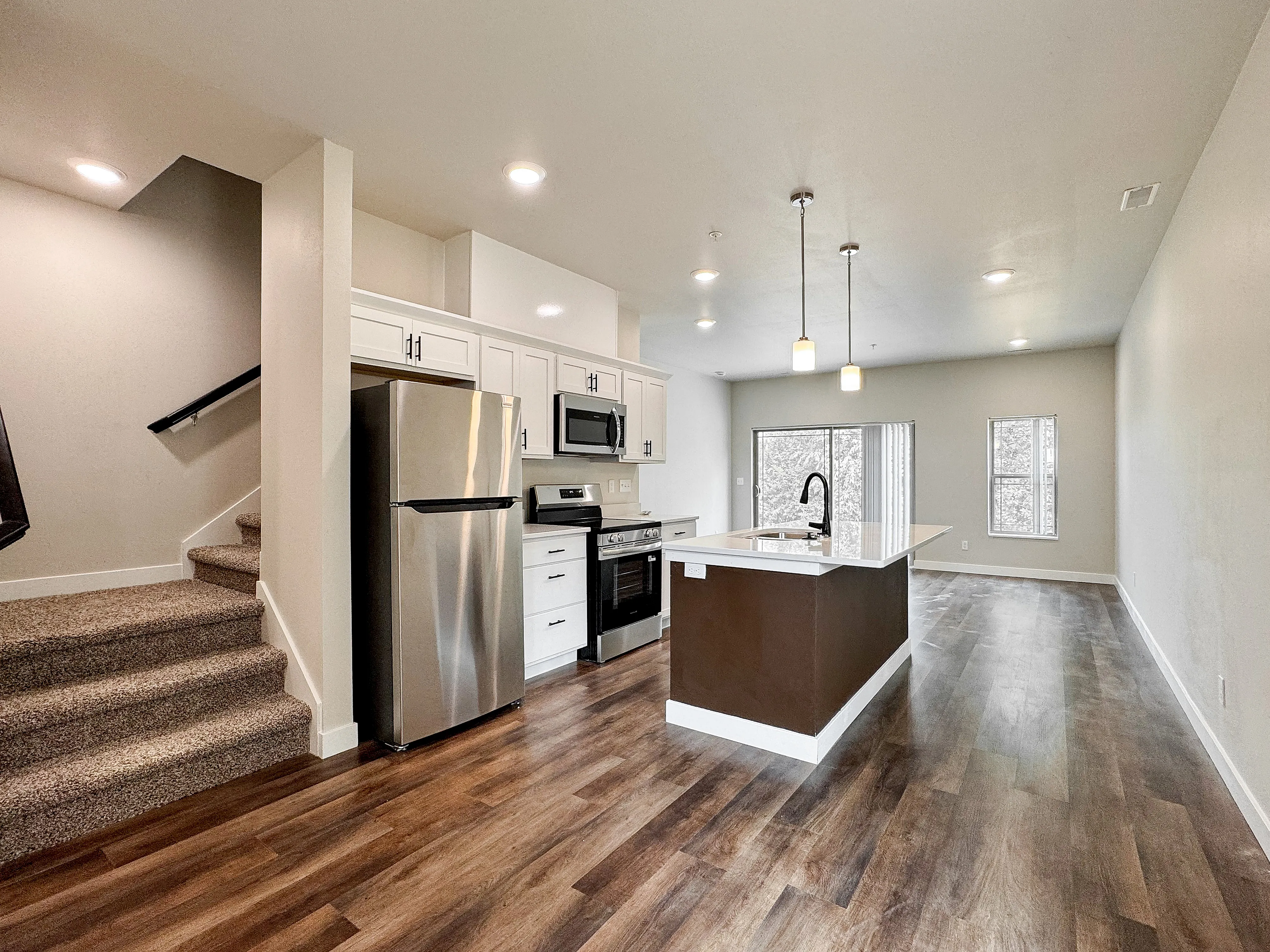 Modern open-concept kitchen in a bright apartment featuring stainless steel appliances, elegant countertops, and chic pendant lighting with stunning wood flooring.