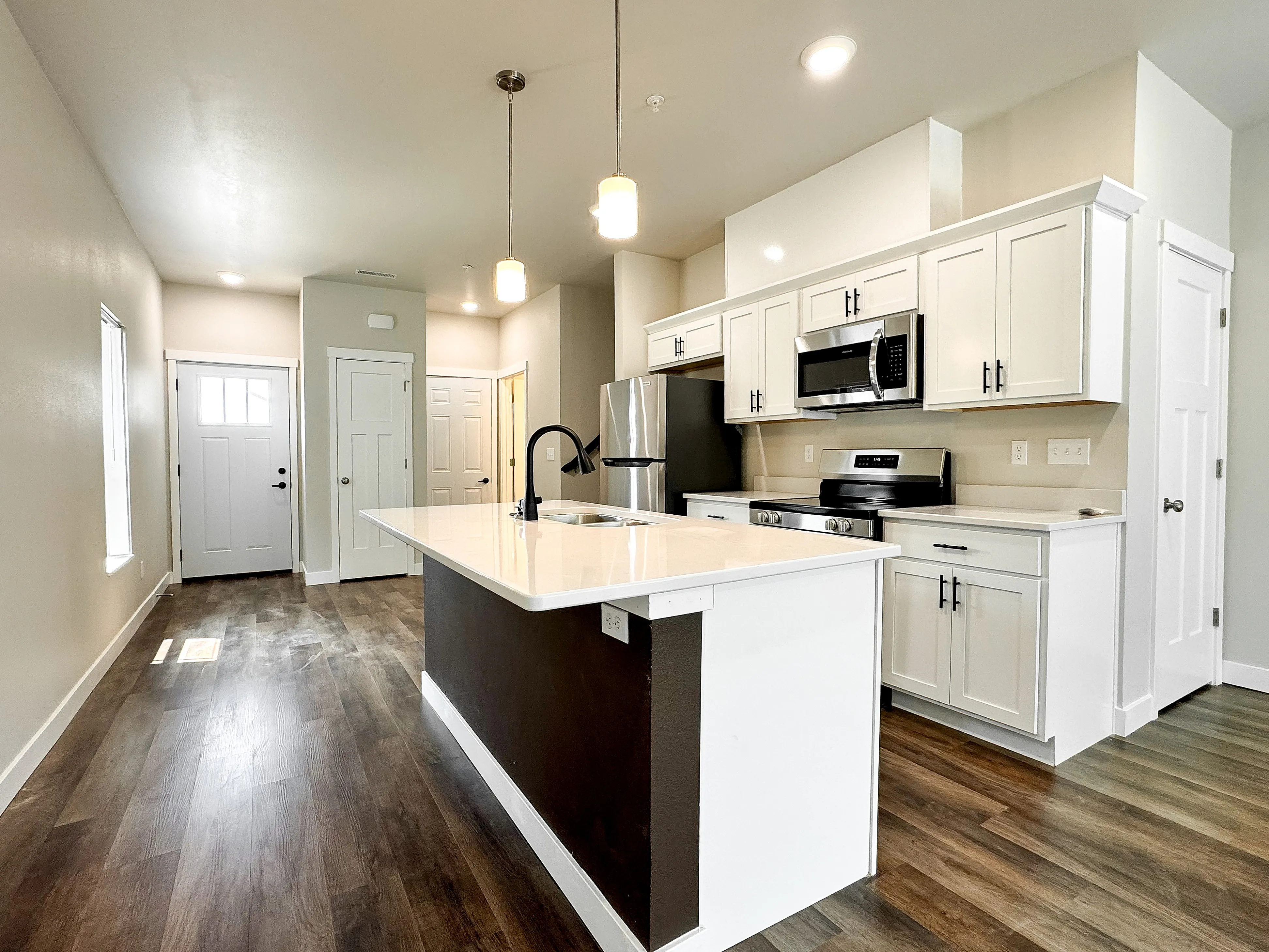 Modern kitchen with sleek white cabinetry, stainless steel appliances, and elegant island under stylish pendant lighting.