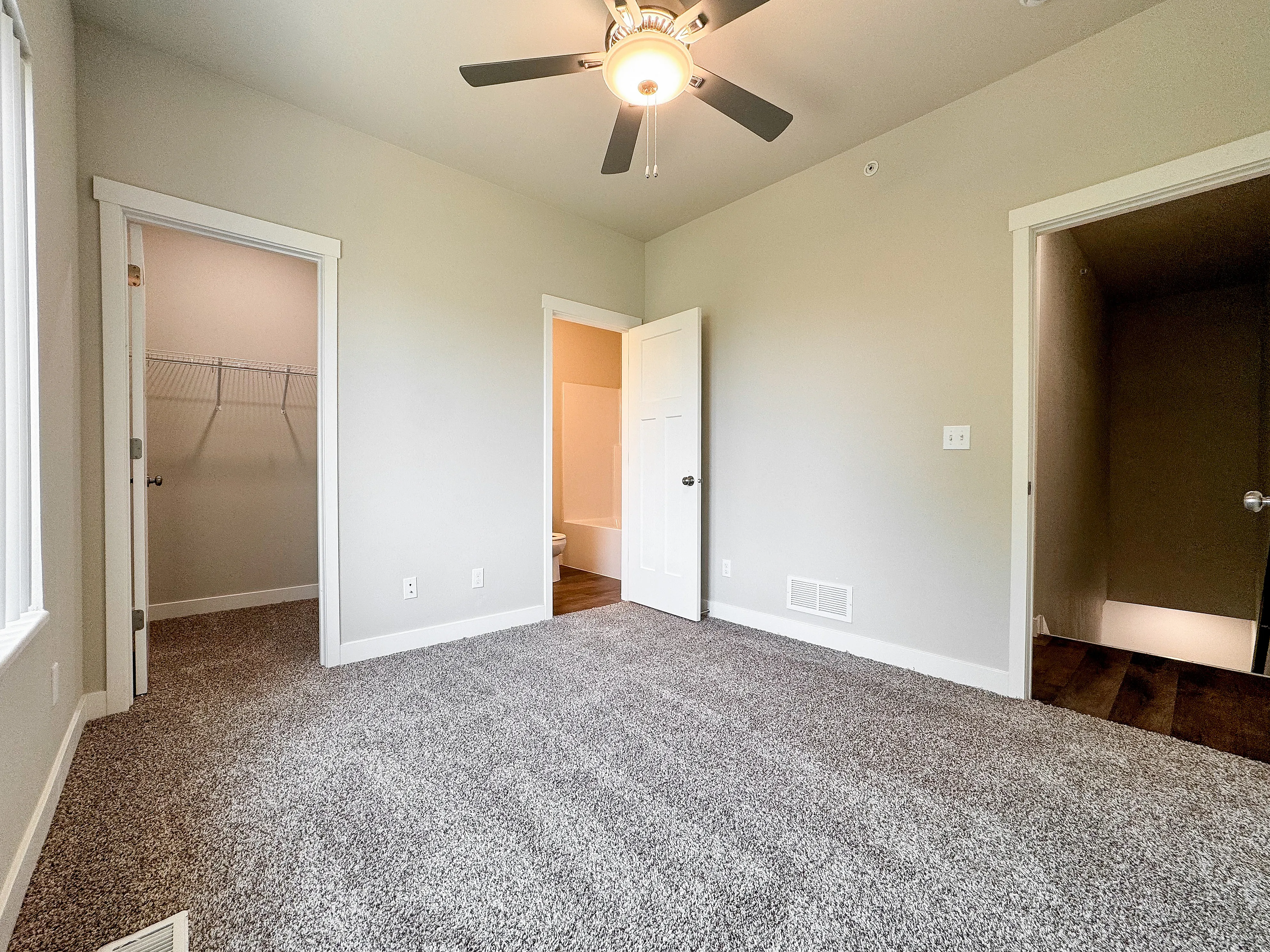 Bright bedroom showcasing plush carpeting, ceiling fan, walk-in closet, and ensuite bath.