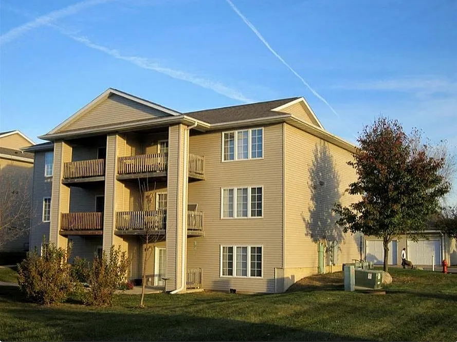 Charming apartment building with private balconies, surrounded by lush greenery and bathed in warm sunlight.
