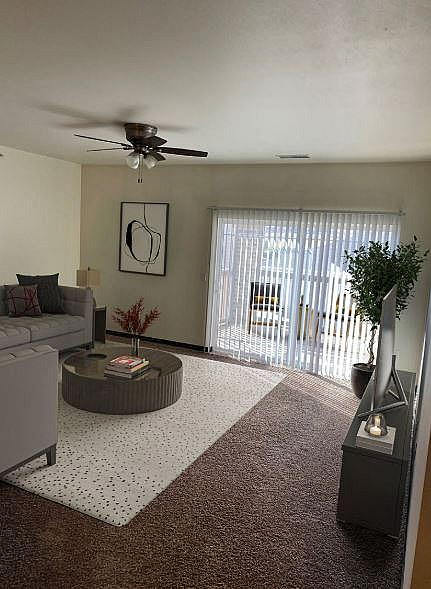 Bright and inviting living room with modern decor, plush carpeting, a stylish ceiling fan, and large sliding glass doors leading to a sunny outdoor space.