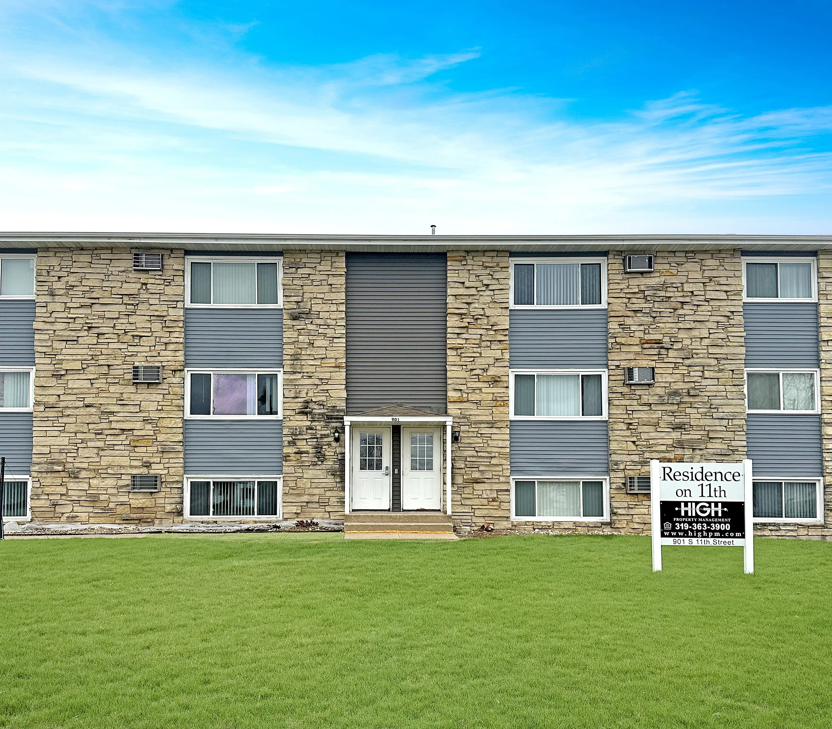 Charming apartment building with modern stone facade and manicured green lawn under a vibrant blue sky, at Residence on 11th.