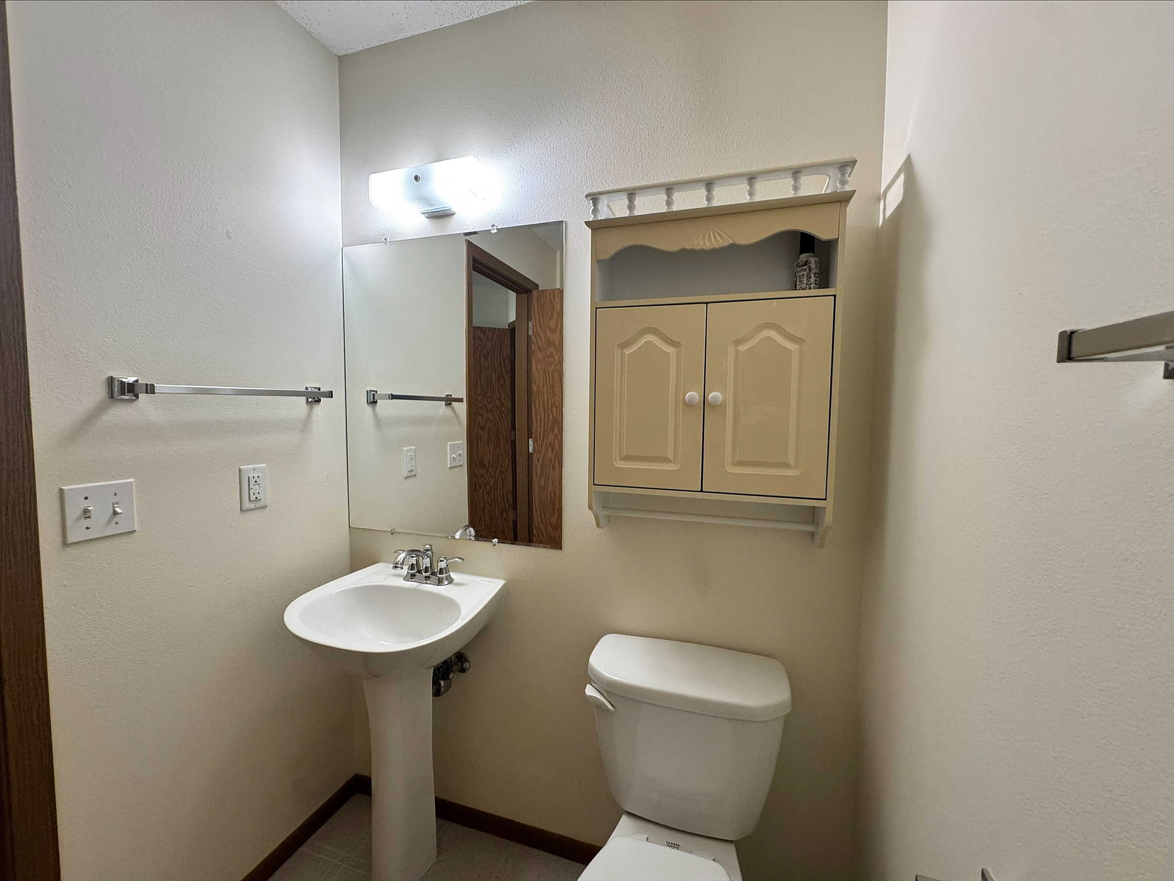 Bright and cozy bathroom featuring a pedestal sink, wall-mounted cabinet, and a large mirror.