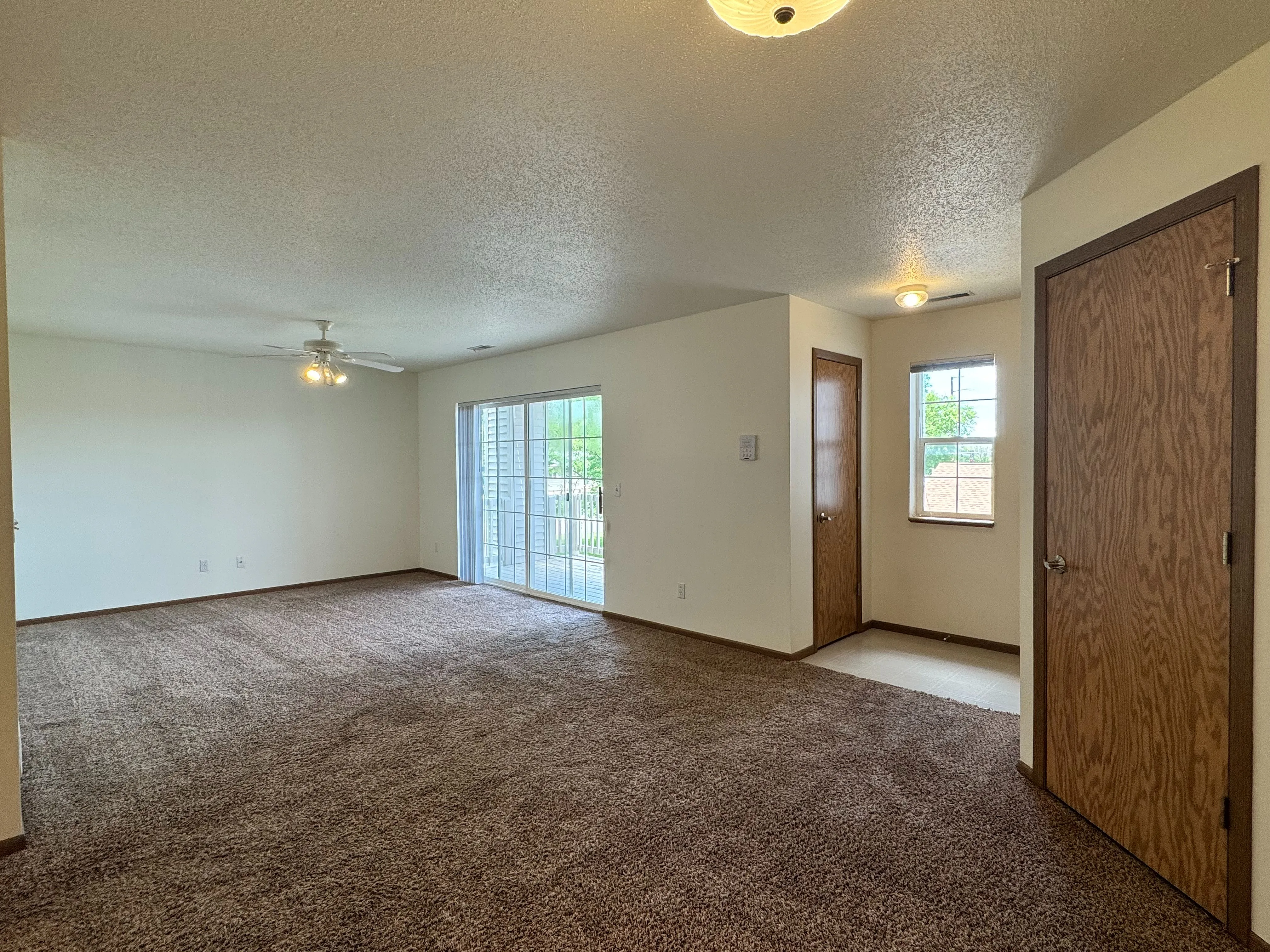 Spacious living area with plush carpeting, natural light through large sliding doors, and cozy ambiance.