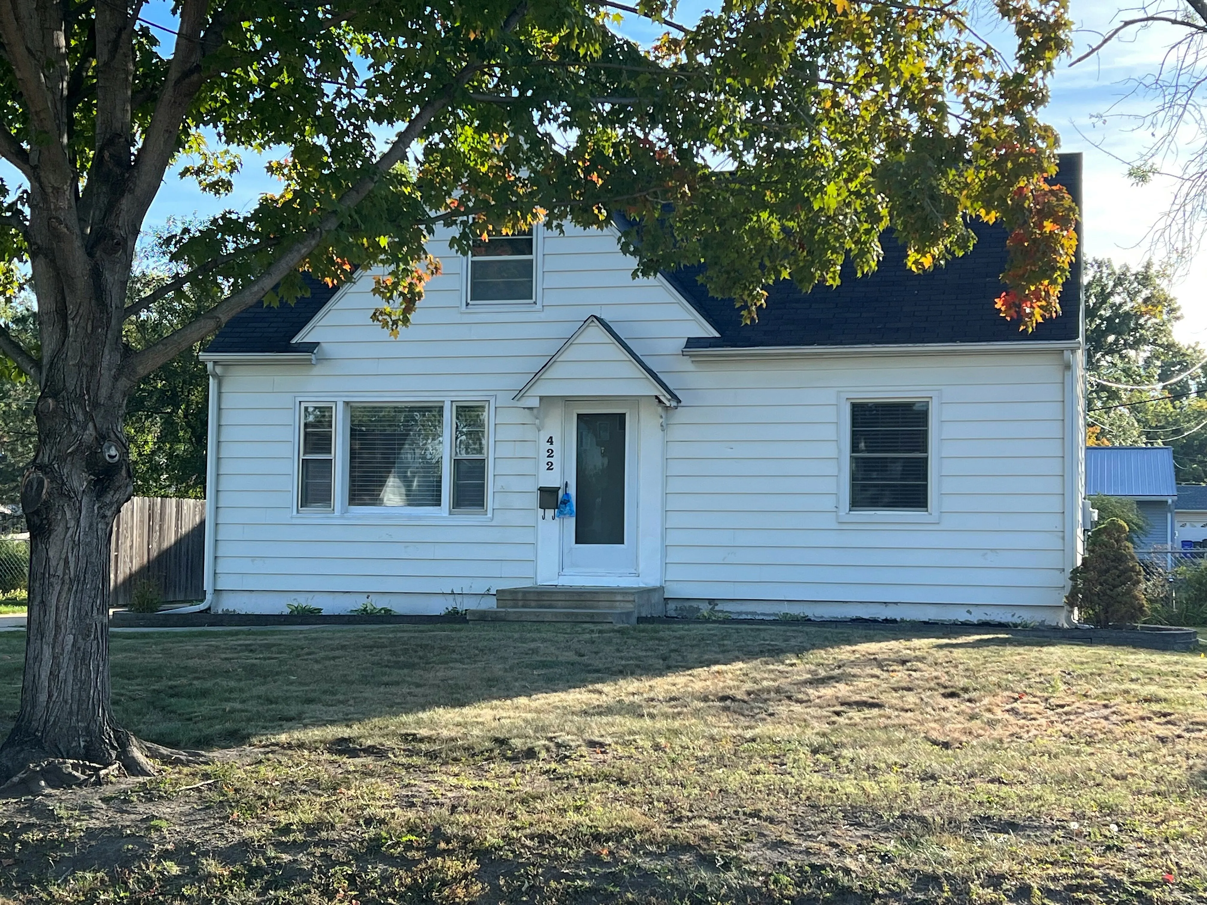 Charming single-story white house with a welcoming entrance and spacious front yard, surrounded by lush greenery and mature trees.