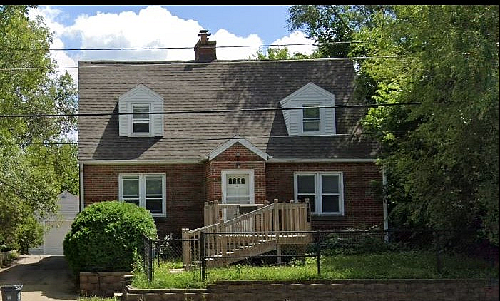 Charming brick house with classic gabled roof, surrounded by lush greenery and featuring a welcoming front porch.