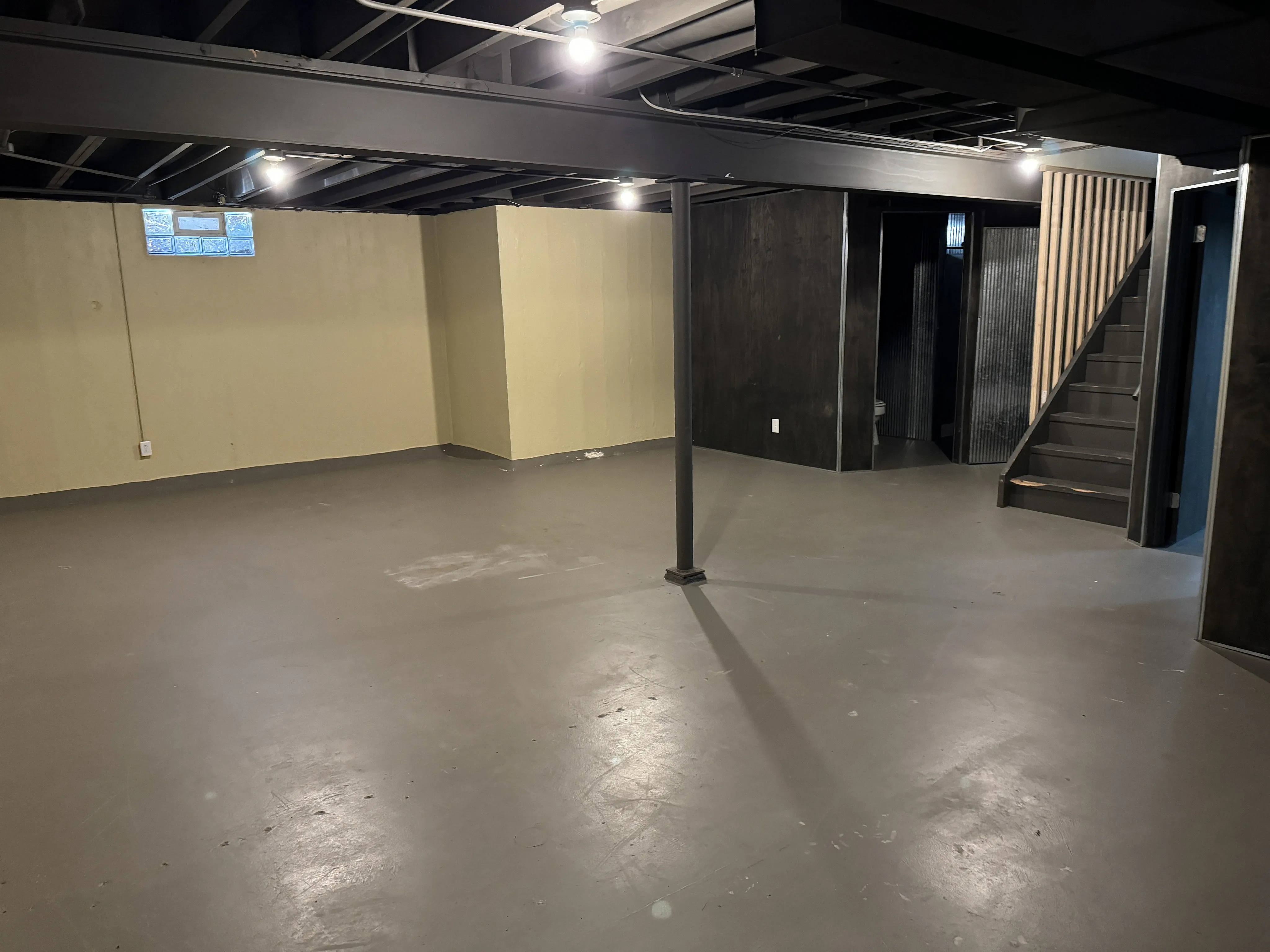 Spacious basement featuring sleek modern design with open area, industrial beams, and stylish staircase access.