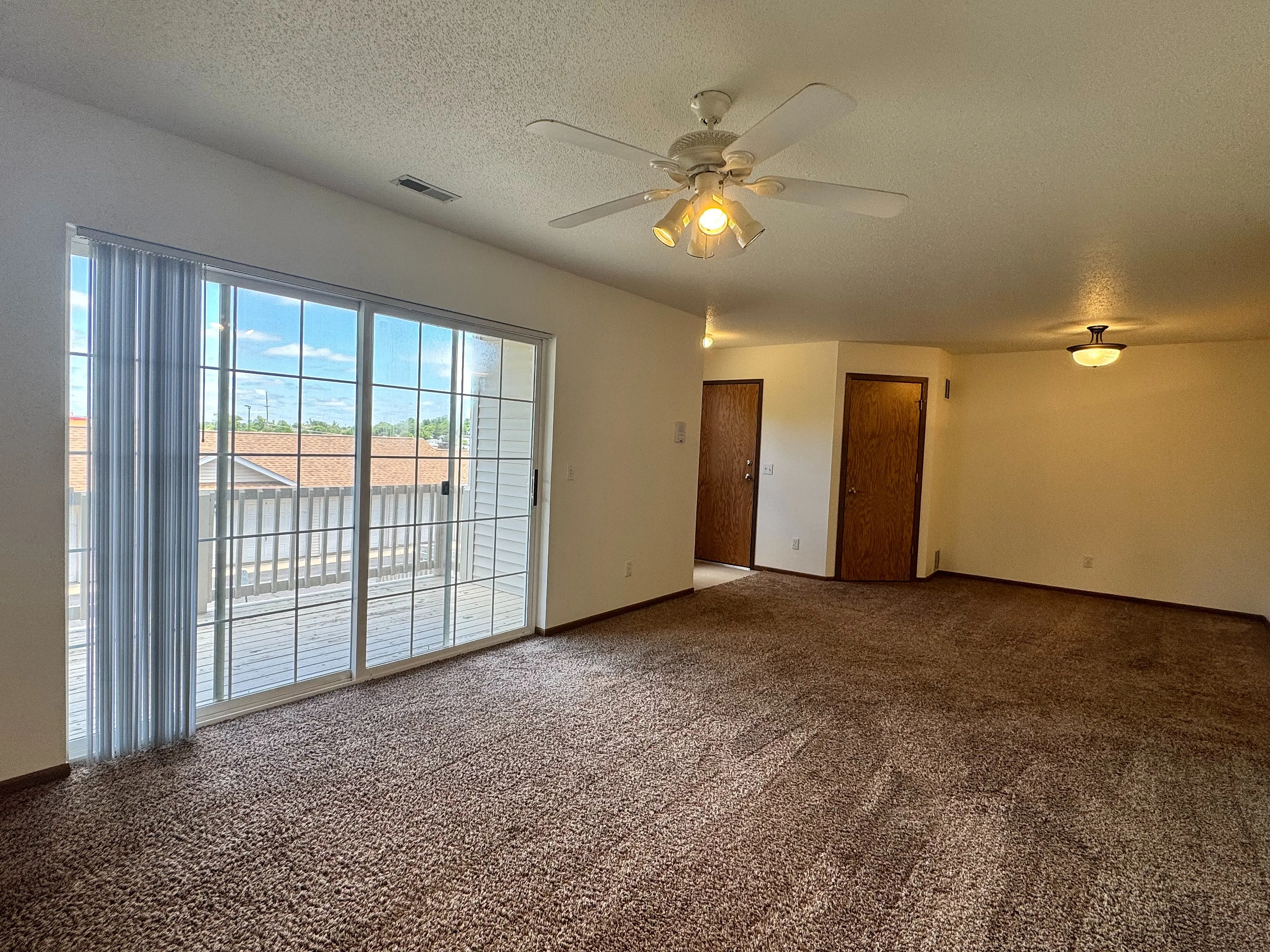 Bright and airy living room with plush carpet and large sliding glass doors opening to a private balcony, perfect for relaxation.