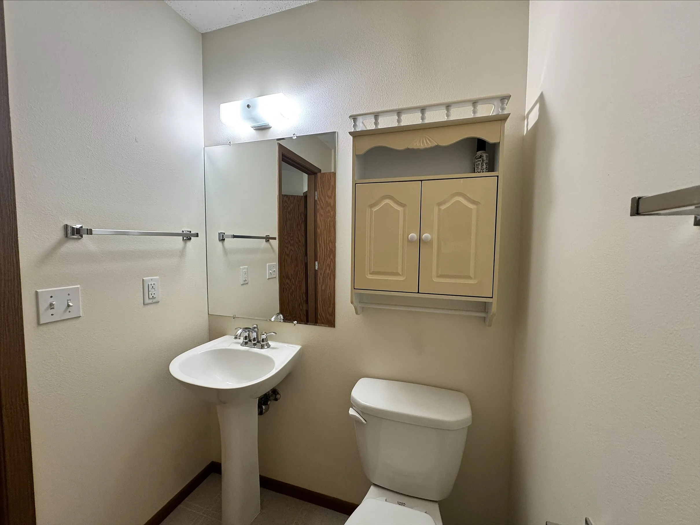 Cozy and bright bathroom with a modern pedestal sink, sleek mirror, and elegant wall cabinet for storage.