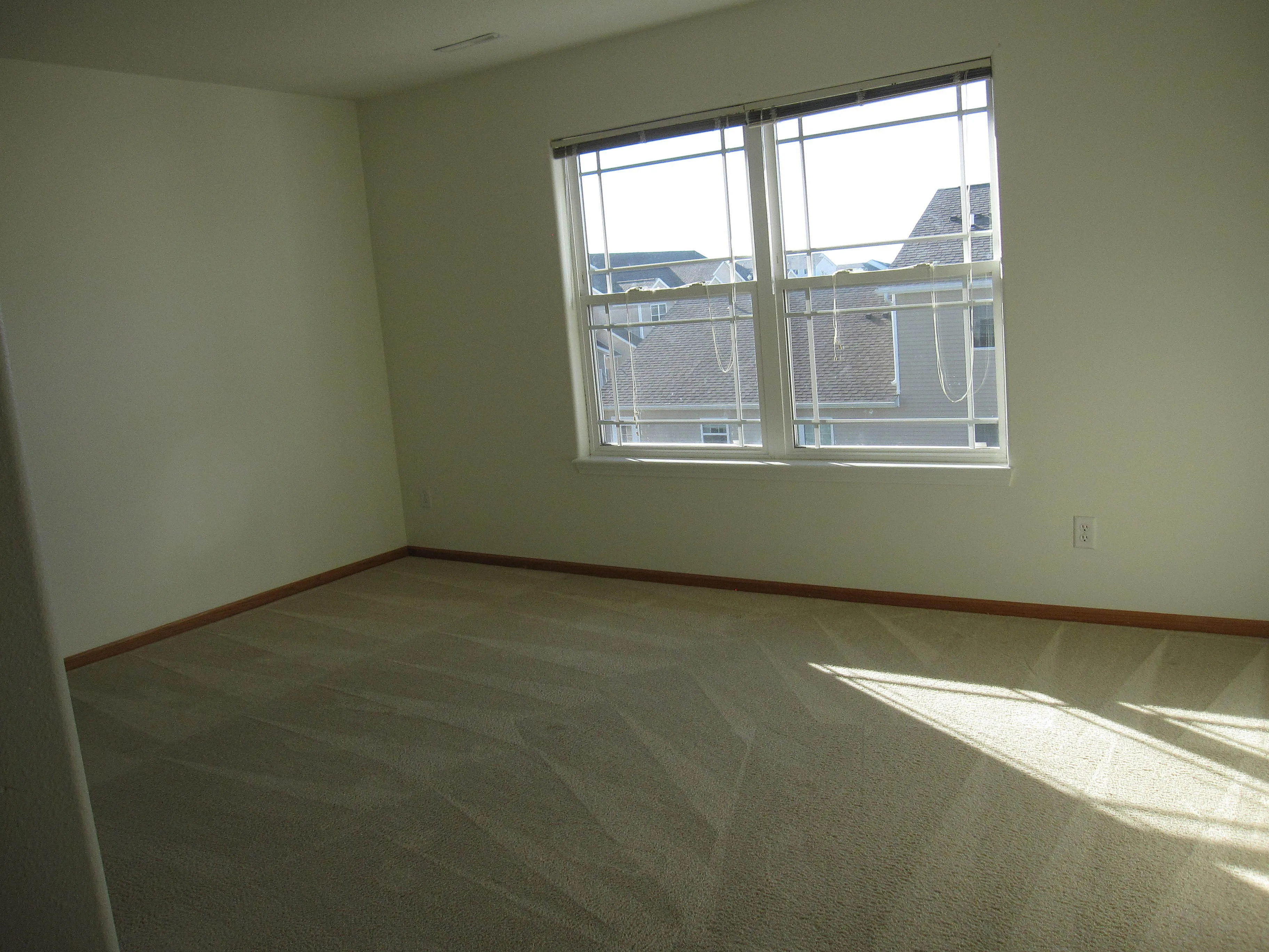 Bright and inviting bedroom with plush carpet, large windows, and a view of charming rooftops.