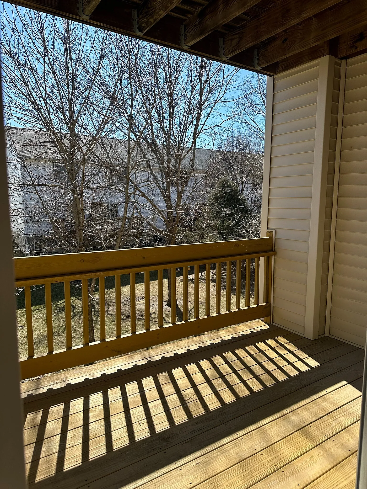 Charming sunlit balcony with wooden railing and scenic view of bare trees, offering a perfect spot for relaxation.
