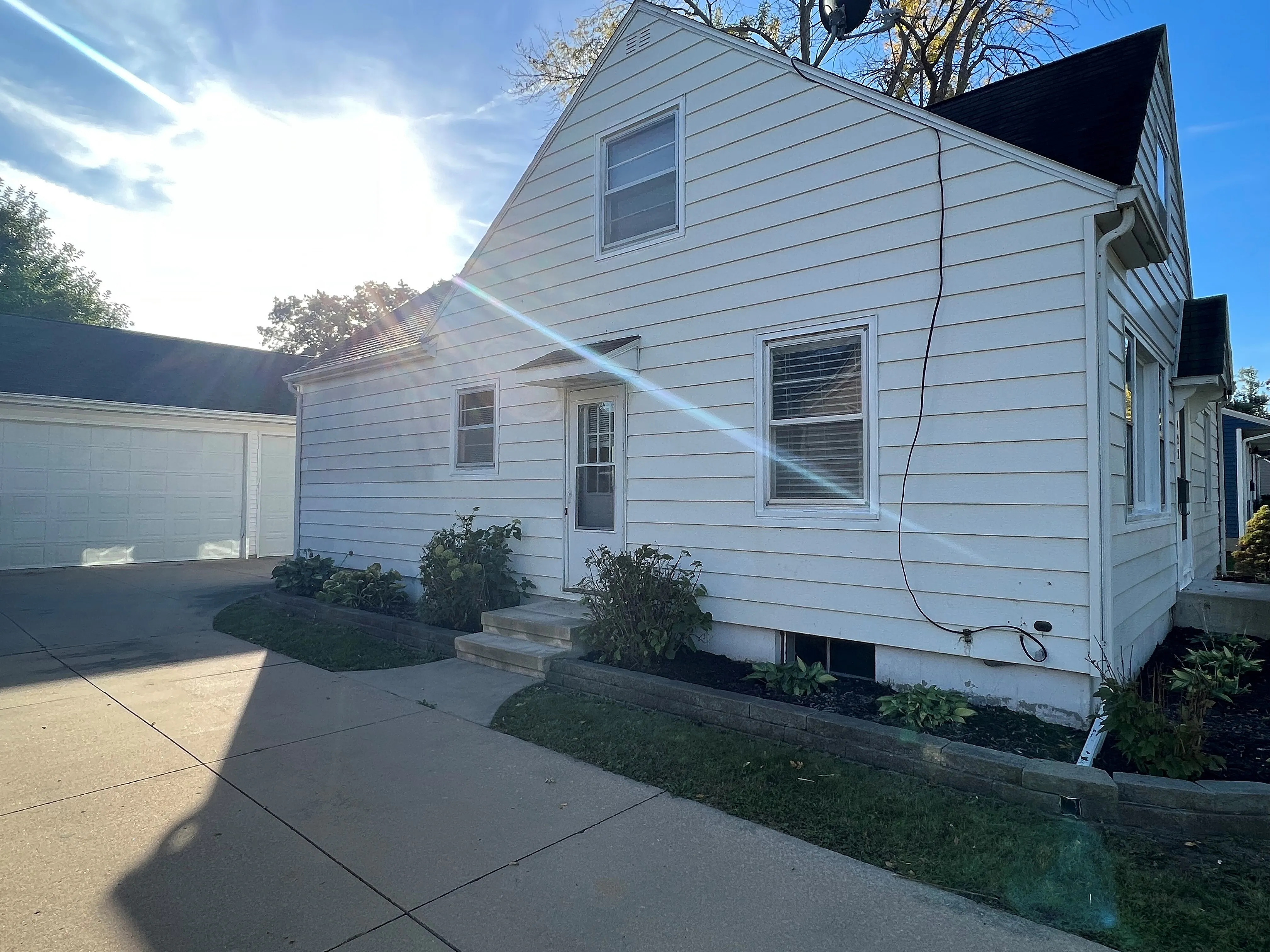 Charming white house with a sunlit front entrance and well-maintained driveway, offering a cozy and inviting atmosphere.