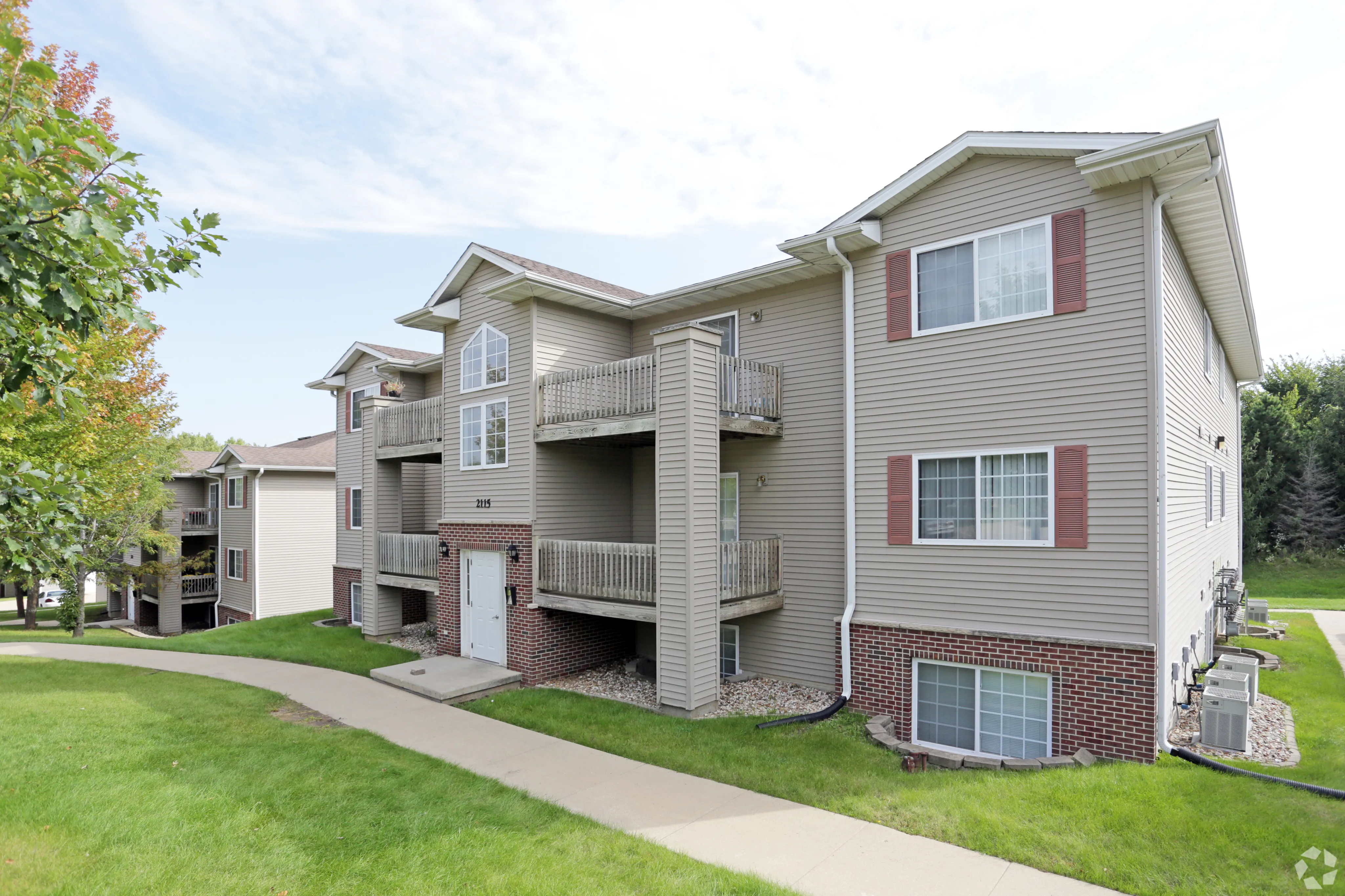 Charming apartment building with spacious balconies, nestled among lush greenery and a peaceful pathway.