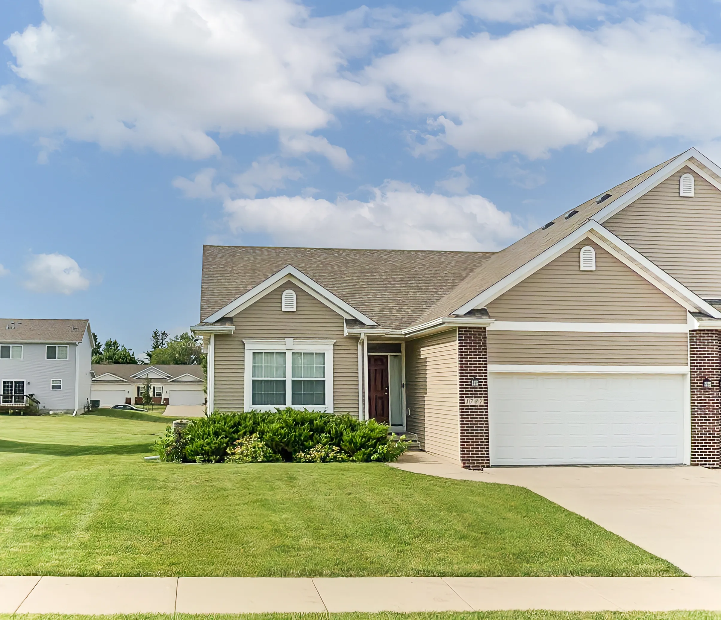 Charming suburban home with a spacious two-car garage, lush green lawn, and inviting entrance under a clear blue sky.