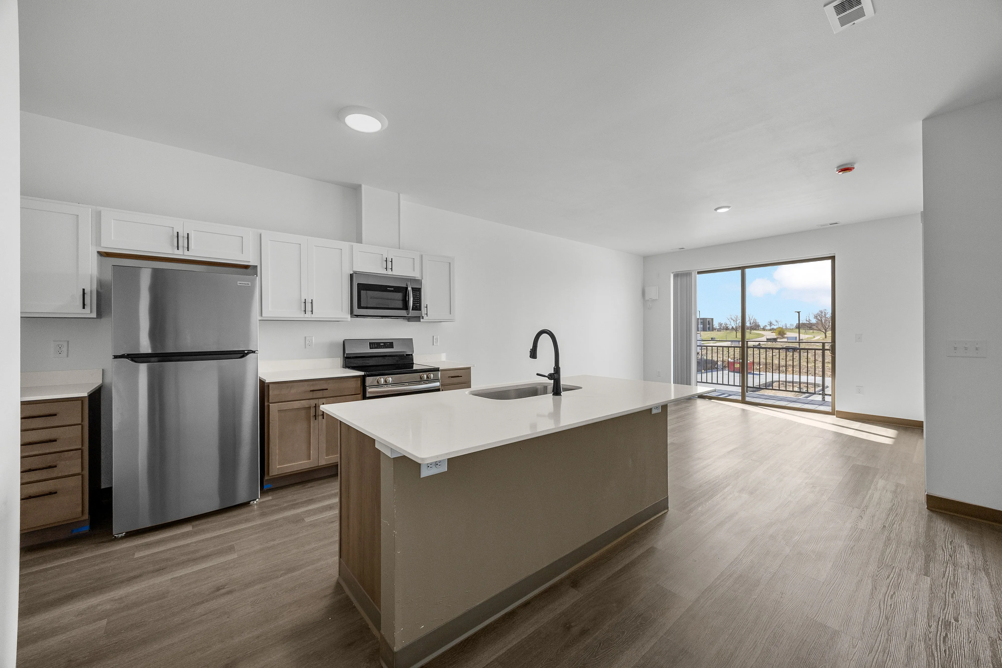 Bright and modern open-plan kitchen with stainless steel appliances, spacious island, and adjacent living area with sliding door access to balcony offering scenic views.