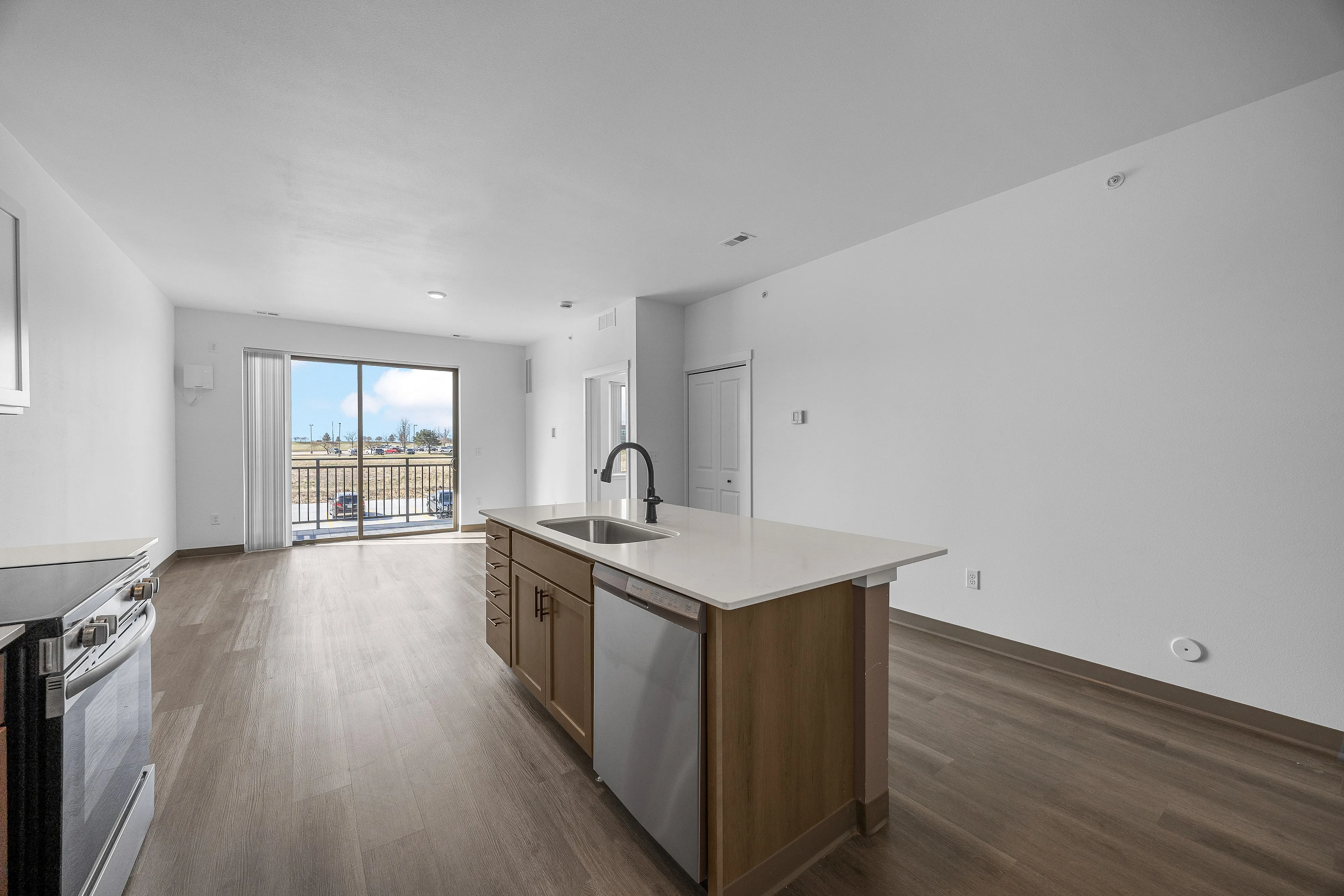 Bright open-concept kitchen with sleek countertops and modern appliances, leading to a spacious living area with large balcony doors and elegant flooring.