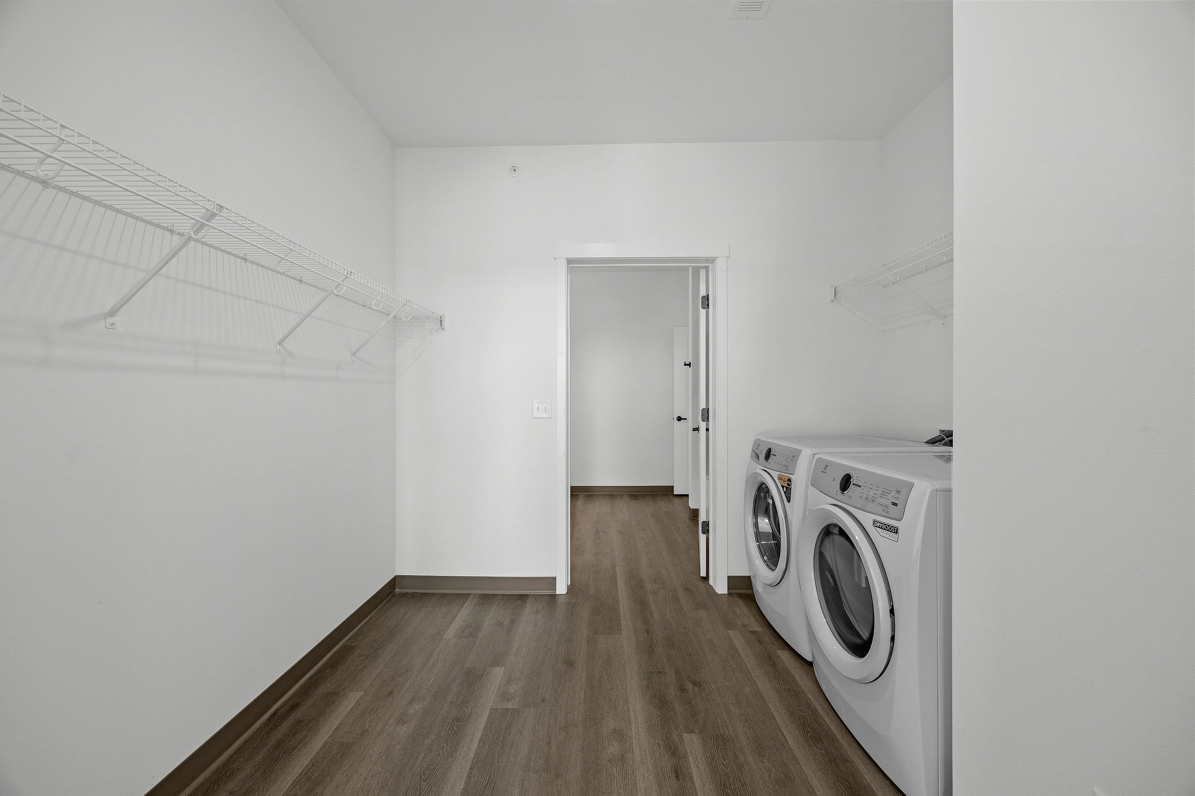 Spacious laundry room with modern washer and dryer, sleek wooden floors, and ample shelving for storage.