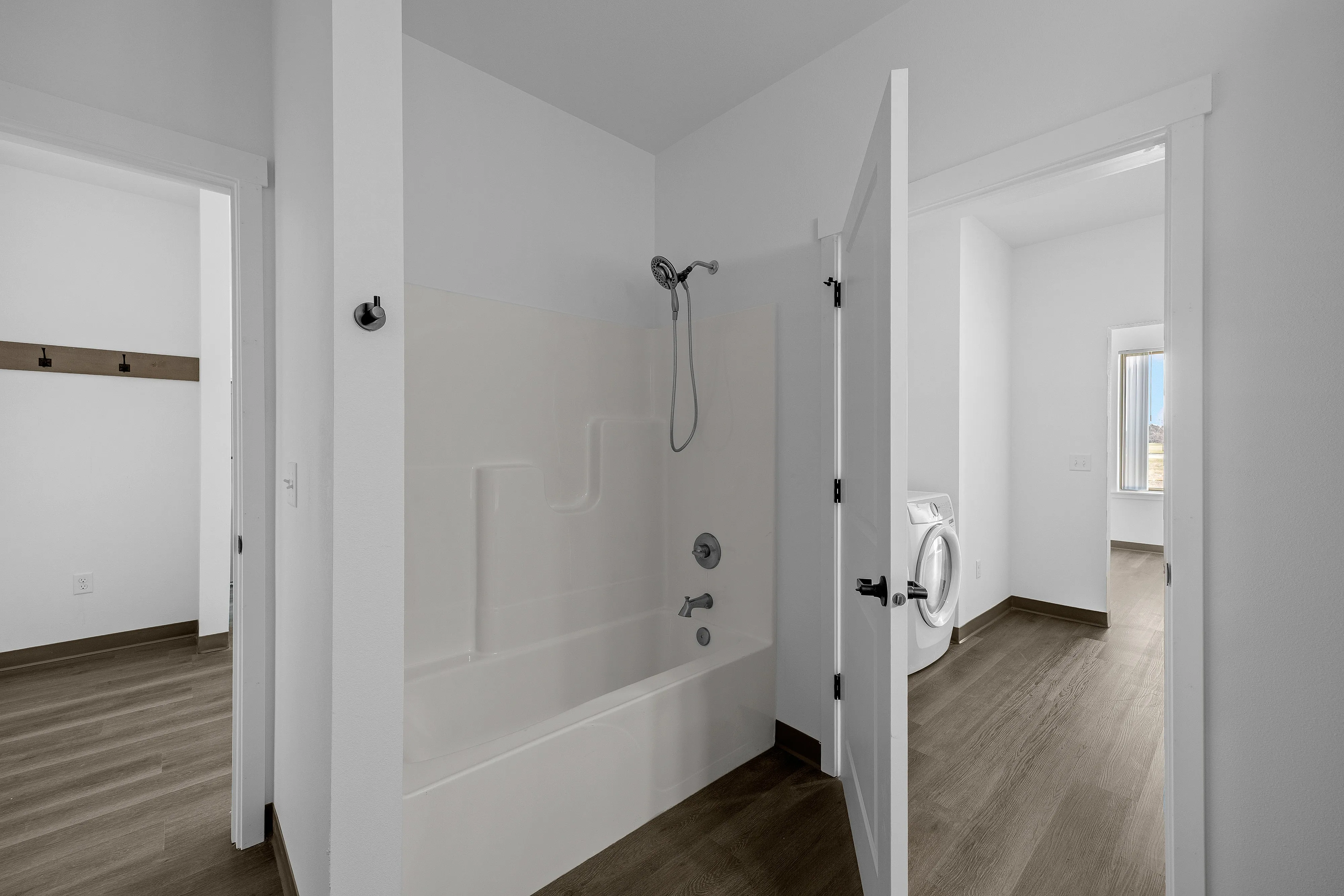 Modern bathroom with sleek tub and shower combo, adjacent laundry room with washer, and bright natural light streaming through the windows.