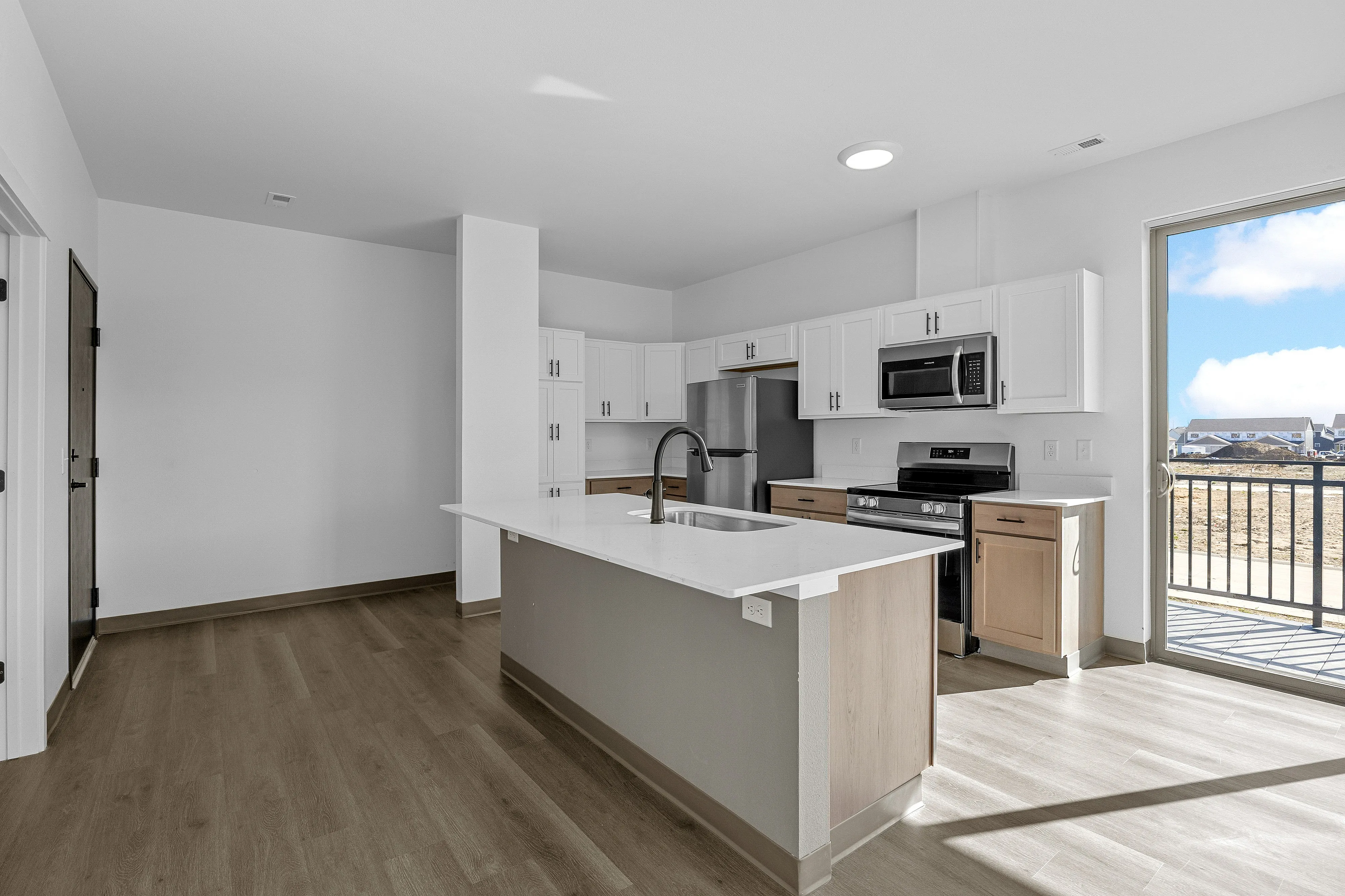 Modern kitchen with sleek white cabinetry, stainless steel appliances, and an elegant island, illuminated by natural light from a large glass door.
