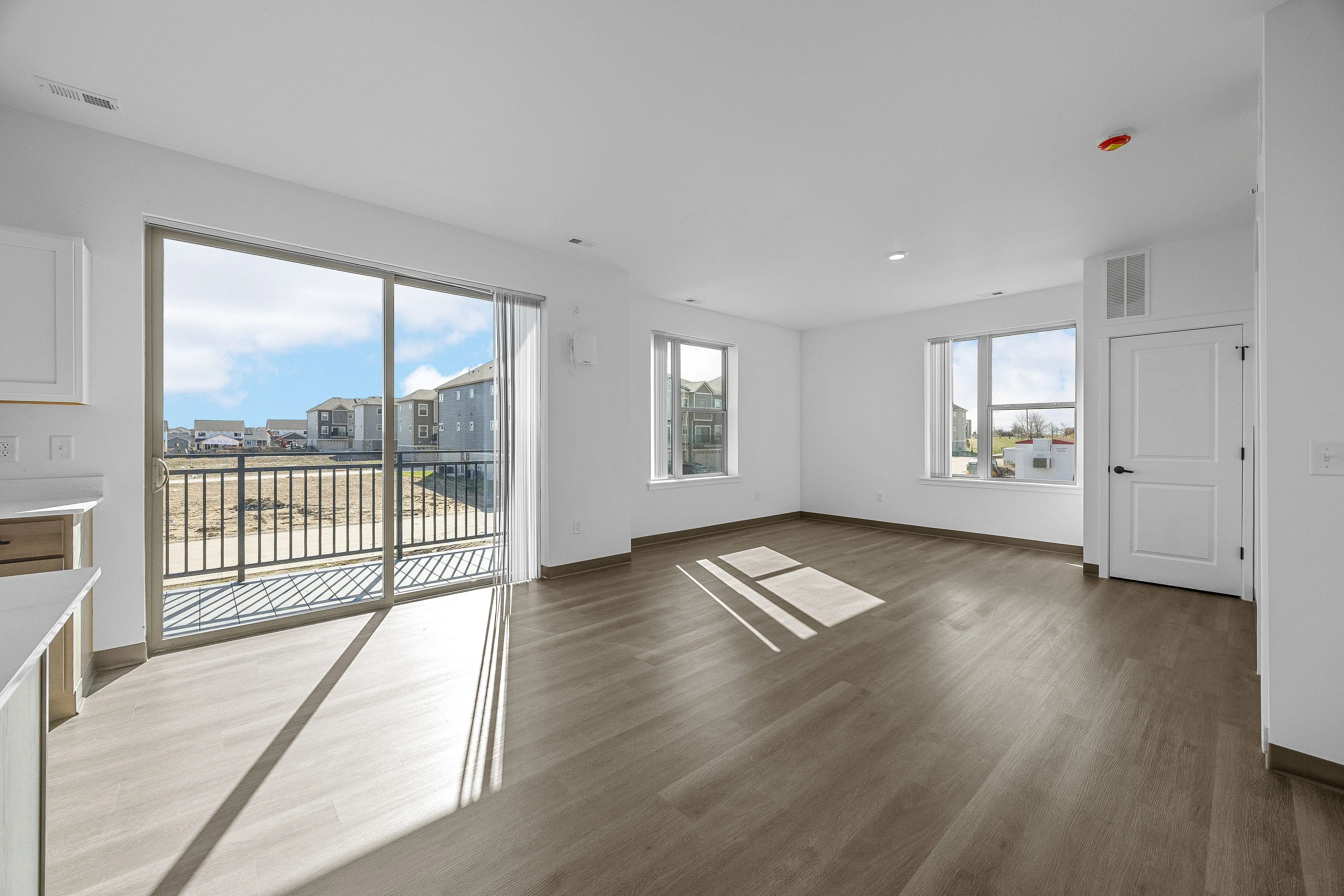 Bright and spacious living area with large windows, wooden flooring, and an inviting balcony view, perfect for modern living.