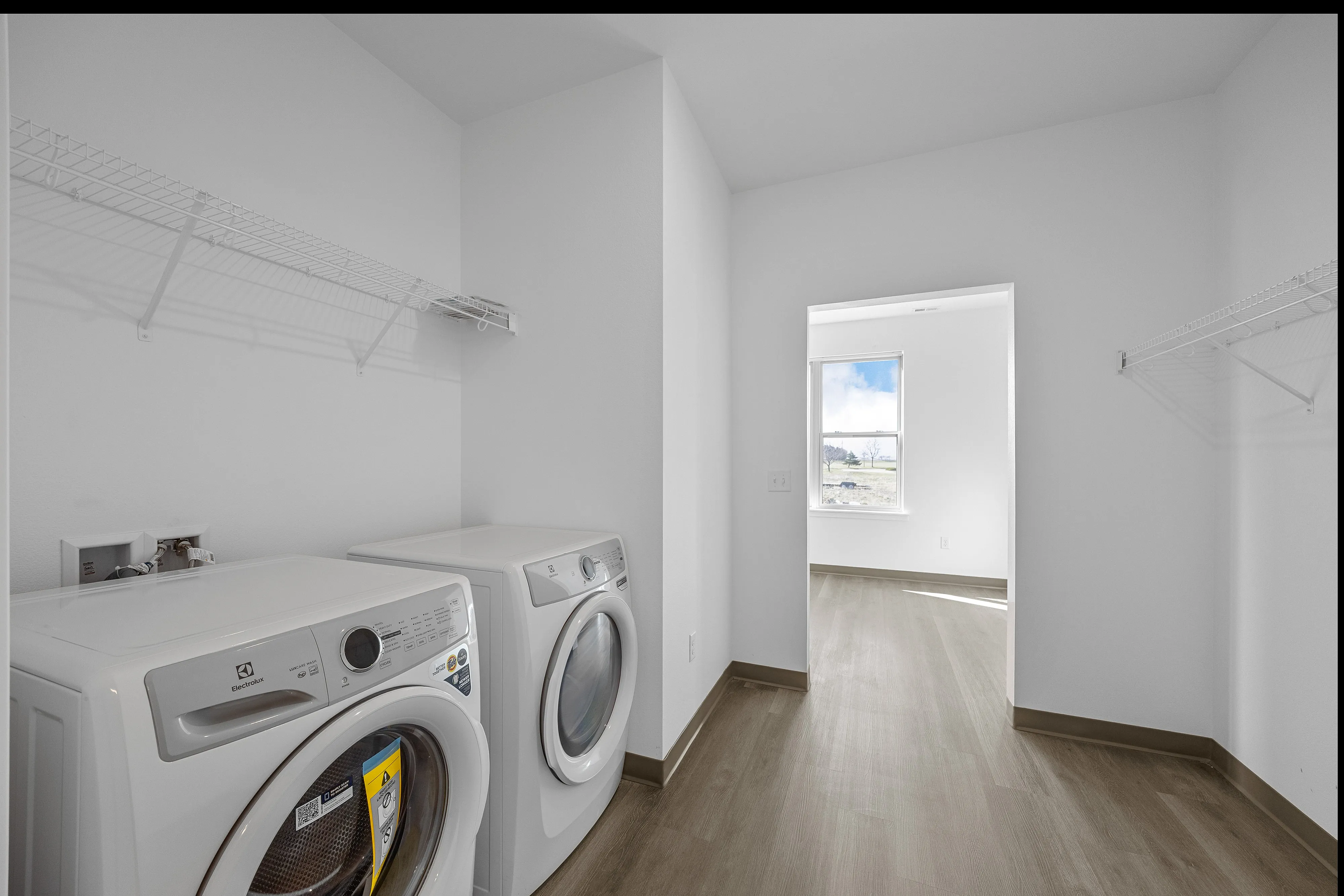 Bright and modern laundry room featuring sleek appliances, airy shelving, and a window with natural light.