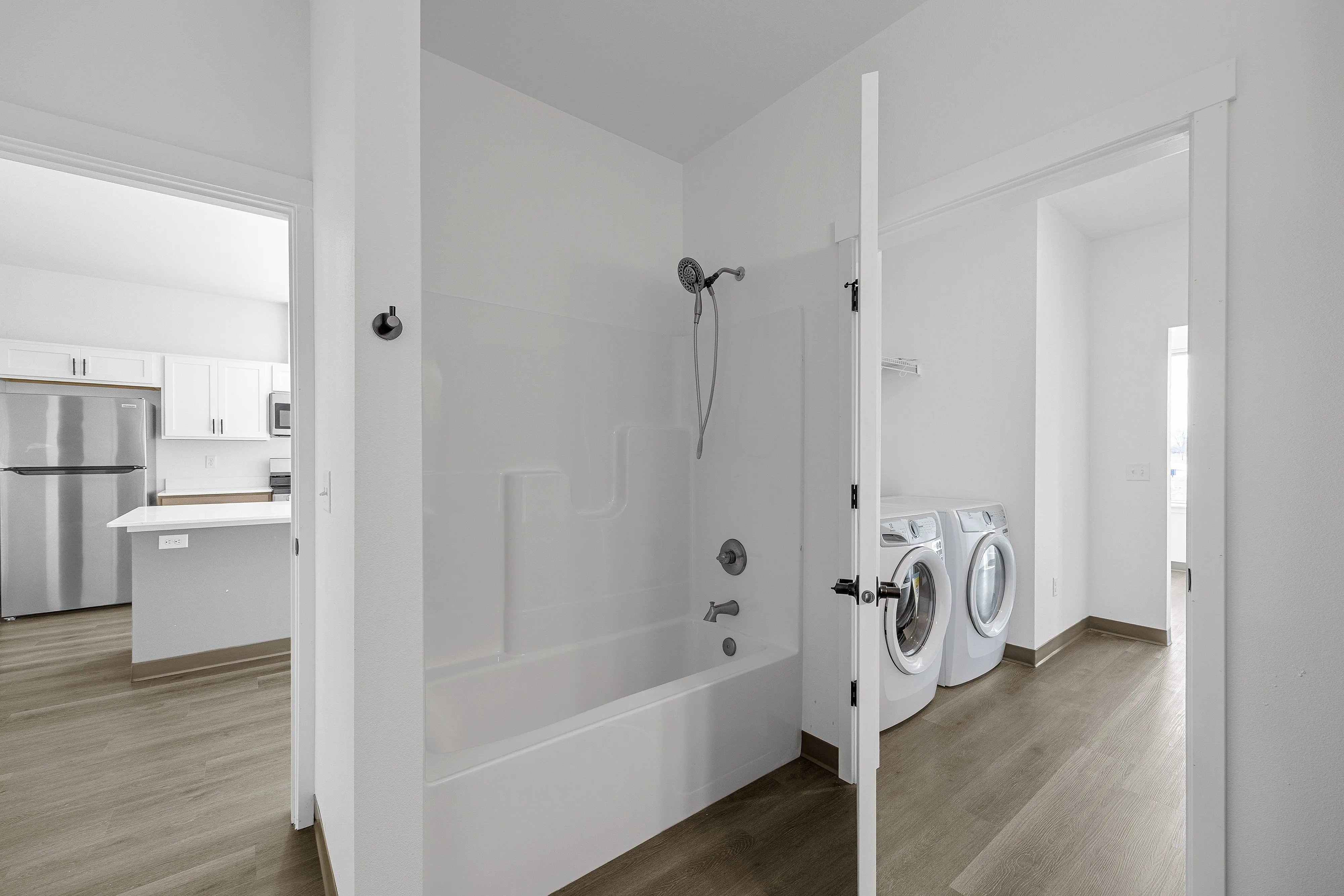 Modern apartment bathroom featuring a pristine bathtub, elegant storage shelves, and a bright laundry room with state-of-the-art washer and dryer.