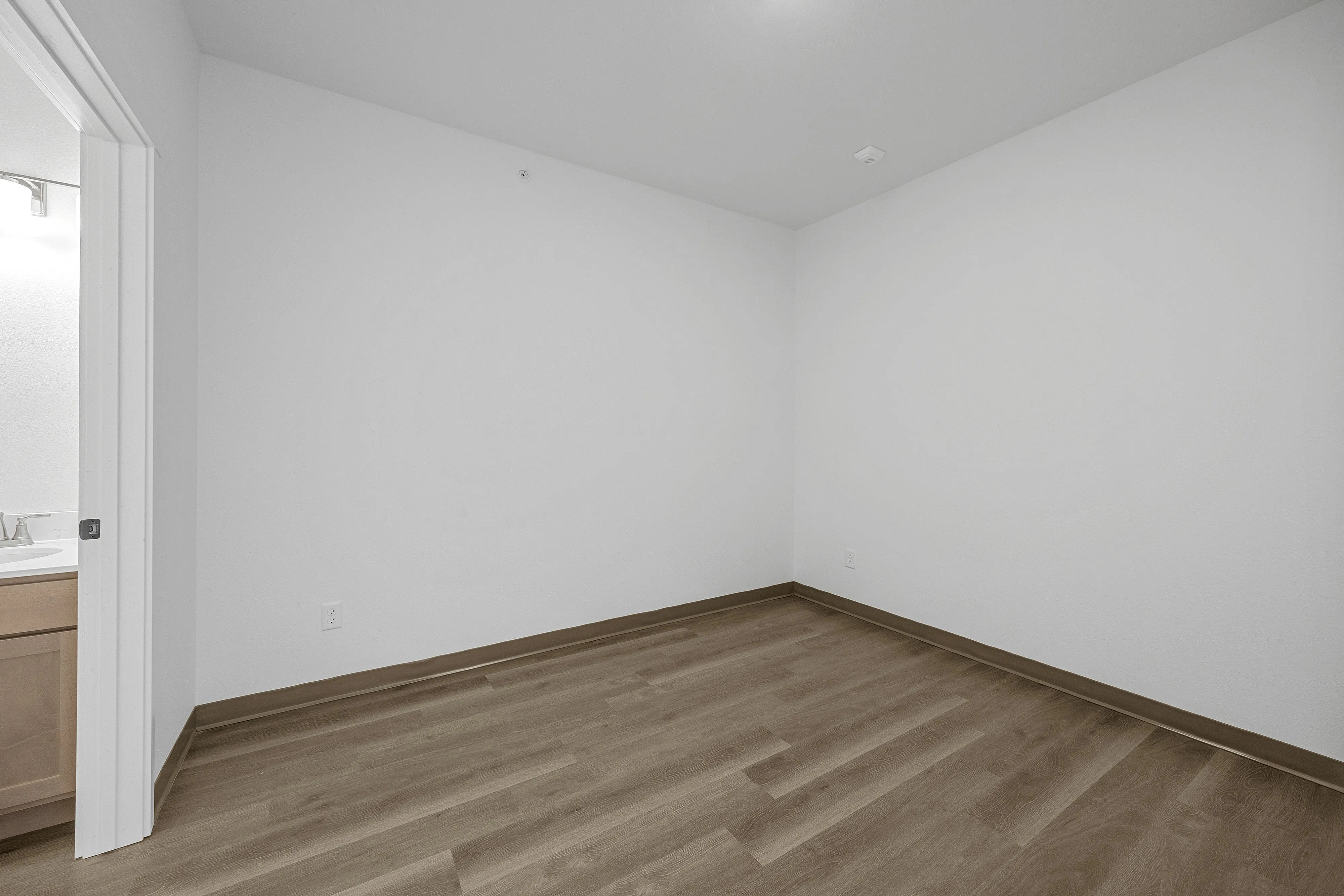 Modern apartment bedroom with sleek wooden flooring and crisp white walls, adjacent to a stylish bathroom.