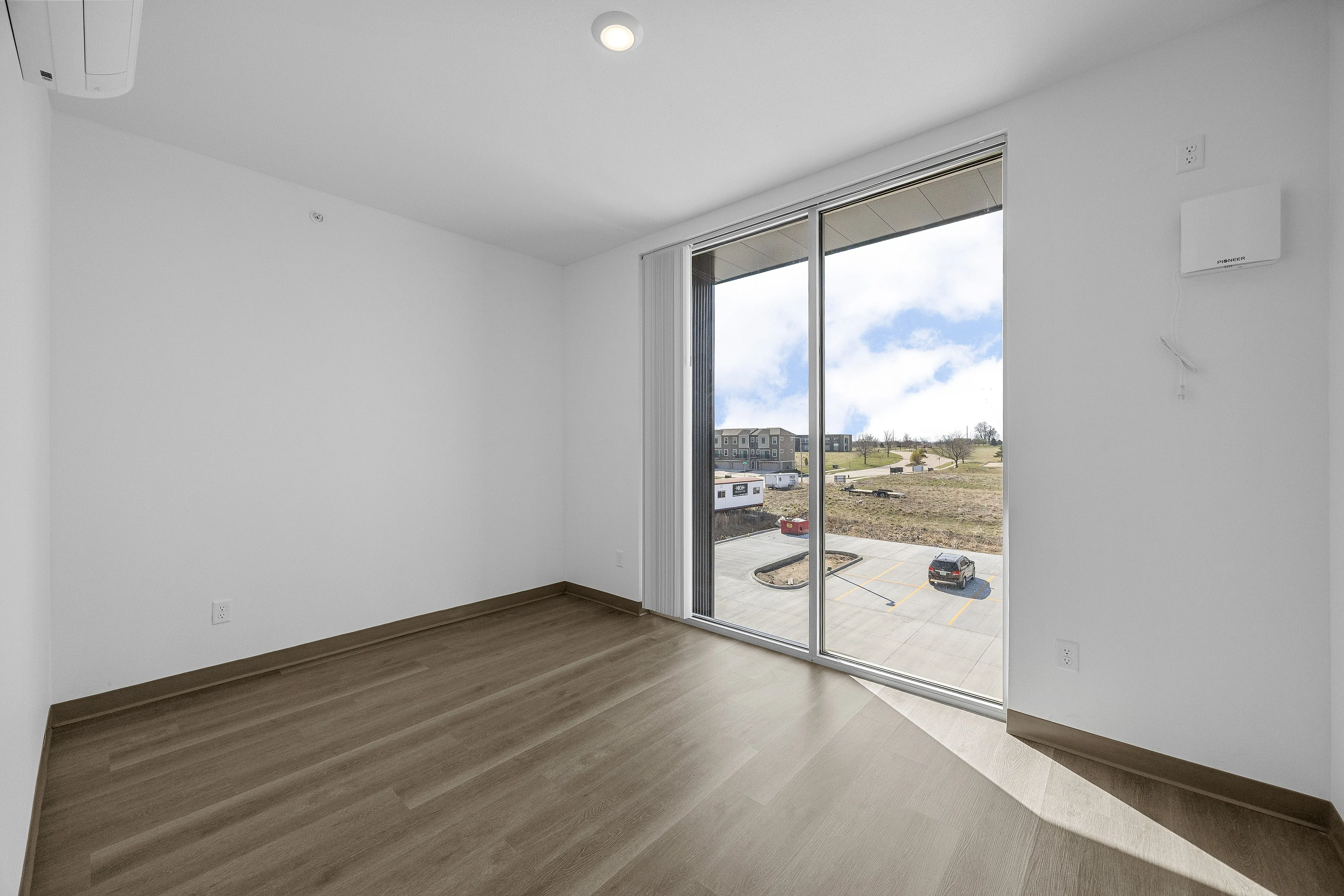 Bright empty room with elegant wood flooring and large sunlit windows offering a scenic outdoor view.