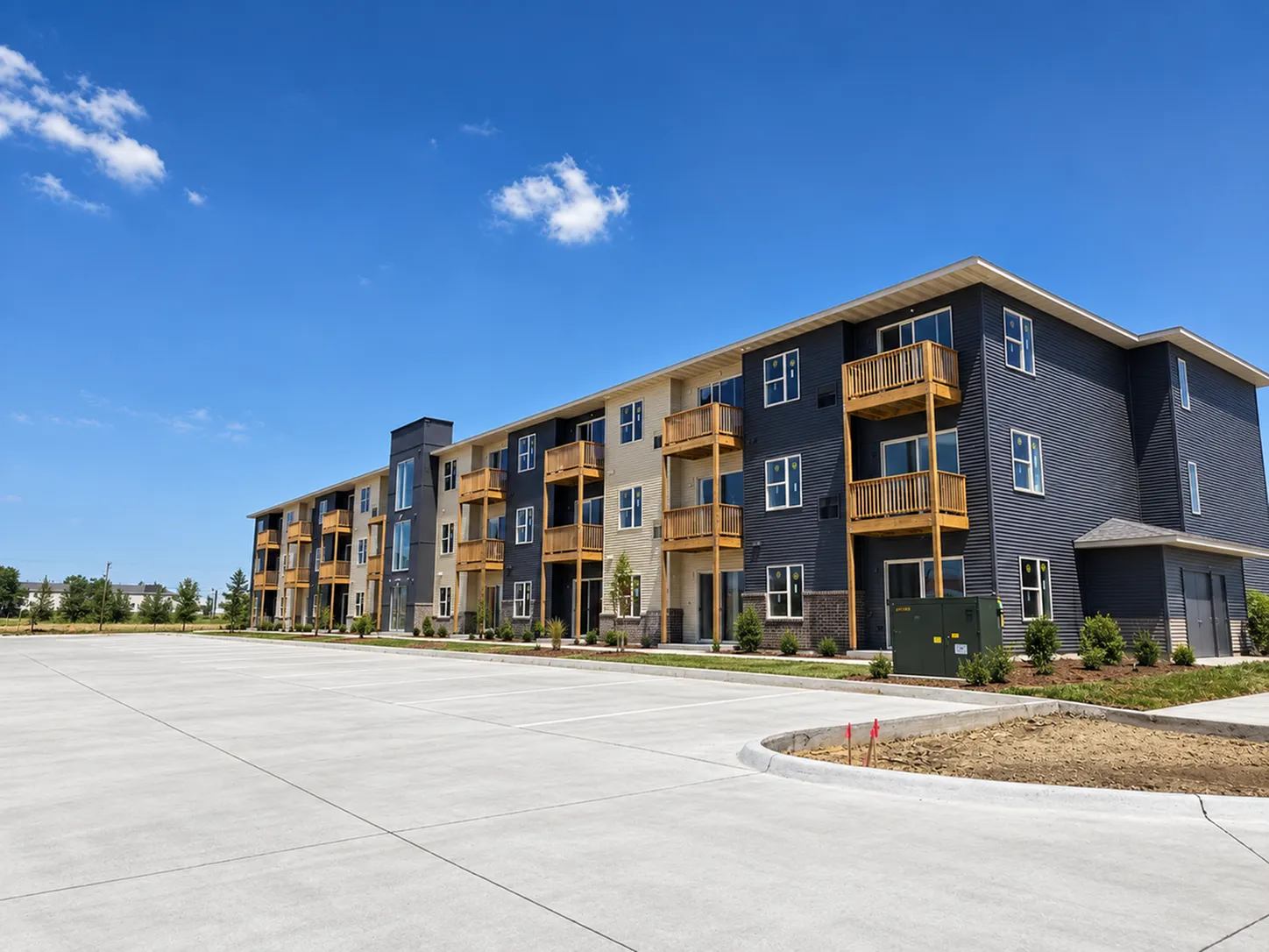 Modern apartment building with sleek exterior design, featuring spacious balconies and surrounded by lush greenery under a clear blue sky.