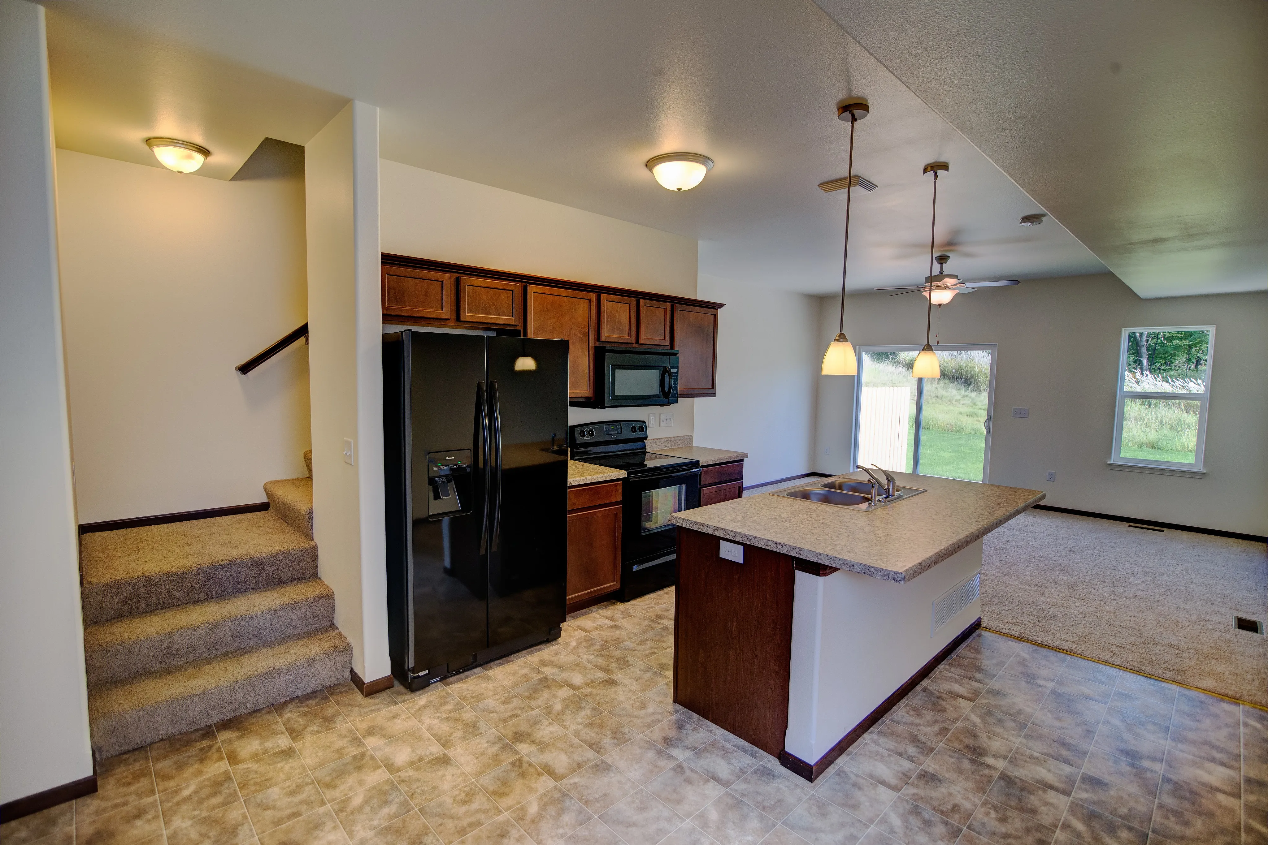Modern open-plan kitchen and living area with elegant lighting, sleek black appliances, and a cozy staircase leading to a serene upstairs view.