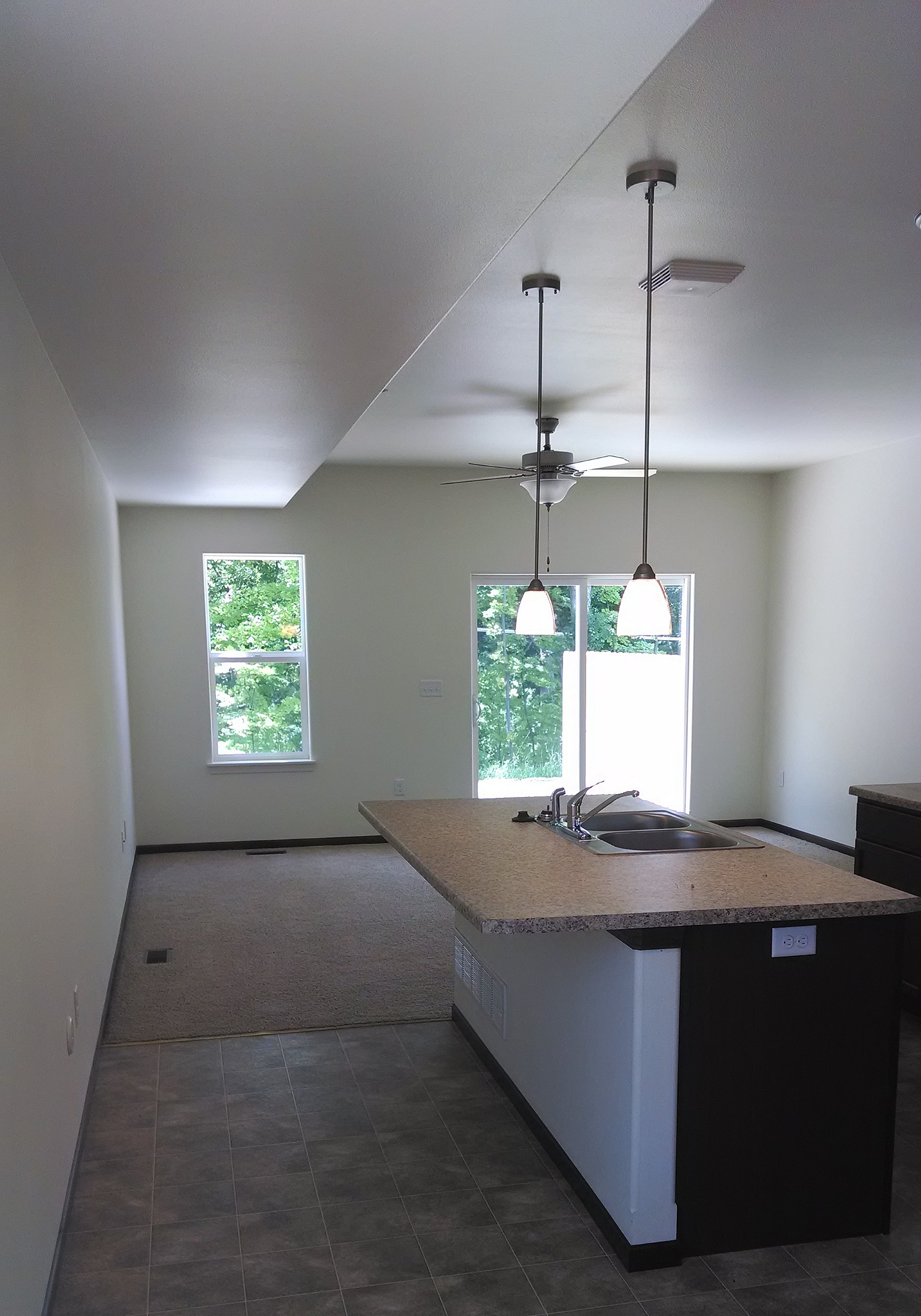 Modern open-concept kitchen and living area with elegant lighting and sleek flooring, featuring a cozy carpeted section with natural light from large windows.