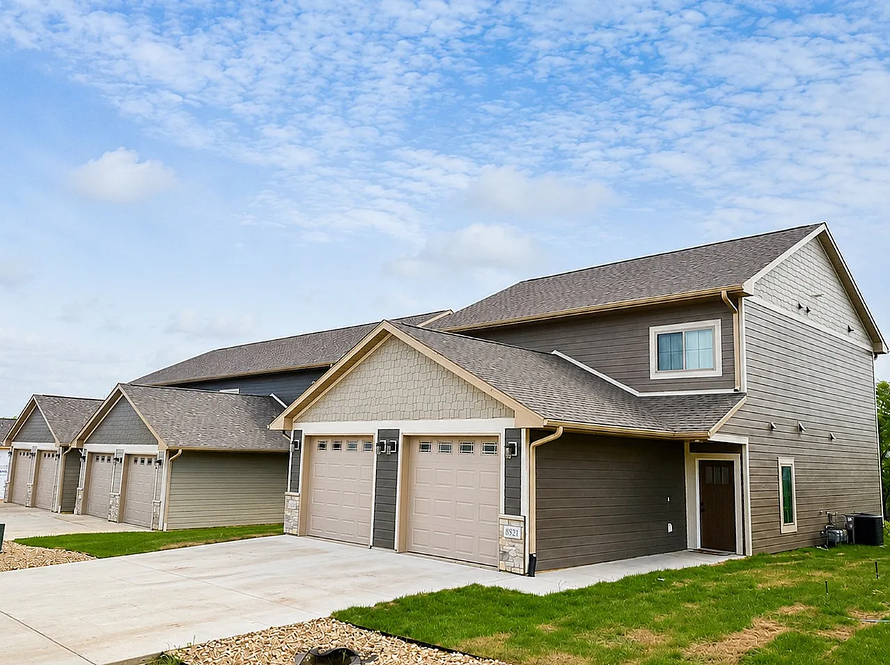 Charming suburban townhouse with a modern exterior, featuring attached garages and neatly landscaped surroundings under a bright blue sky.