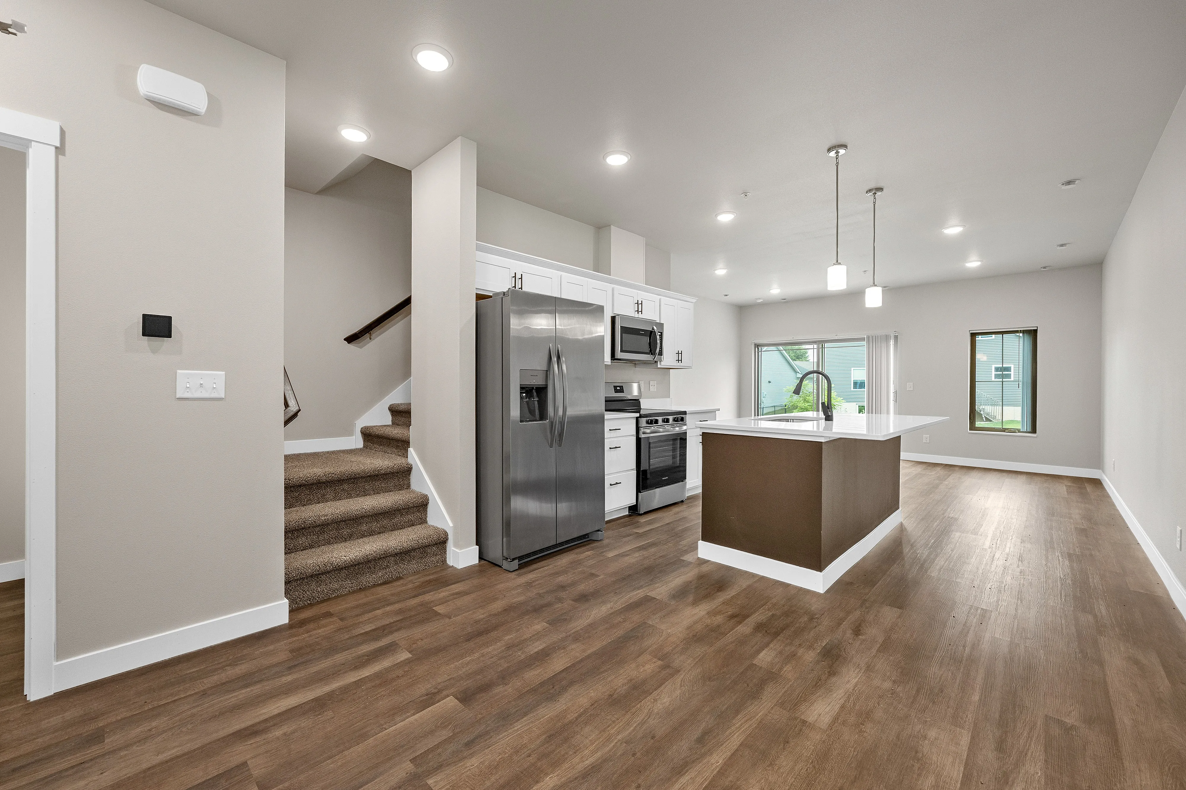 Modern apartment showcasing a sleek kitchen with stainless steel appliances, elegant pendant lighting, and an inviting open-concept living space on rich wooden floors.