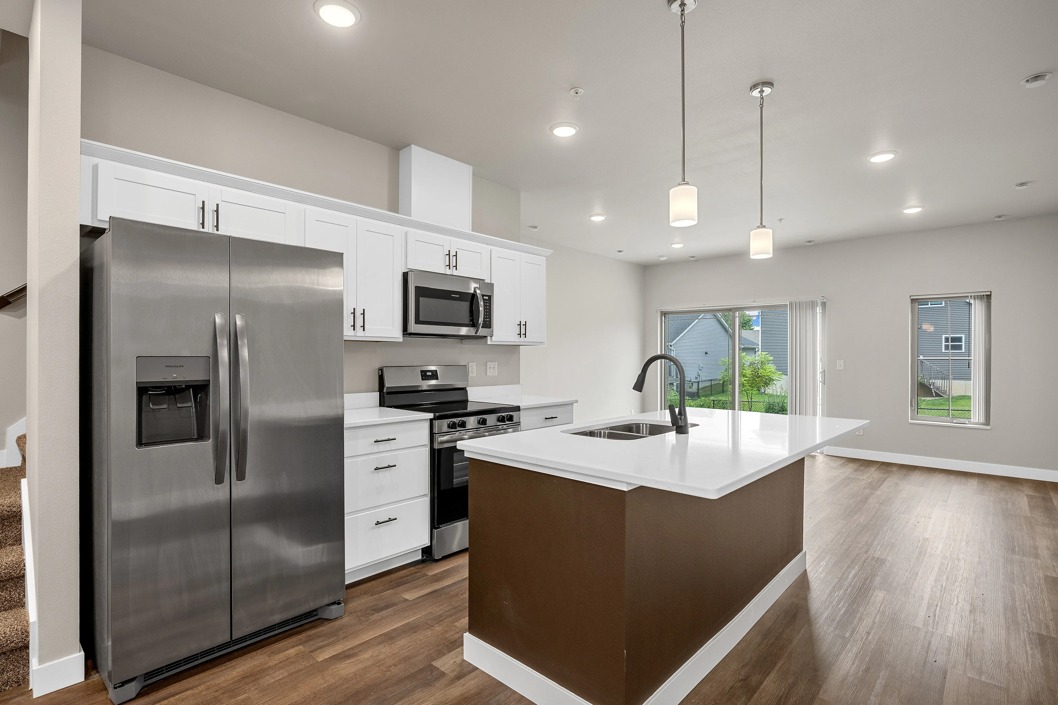 Modern kitchen with sleek stainless steel appliances, an elegant island with pendant lighting, and ample natural light from large windows.