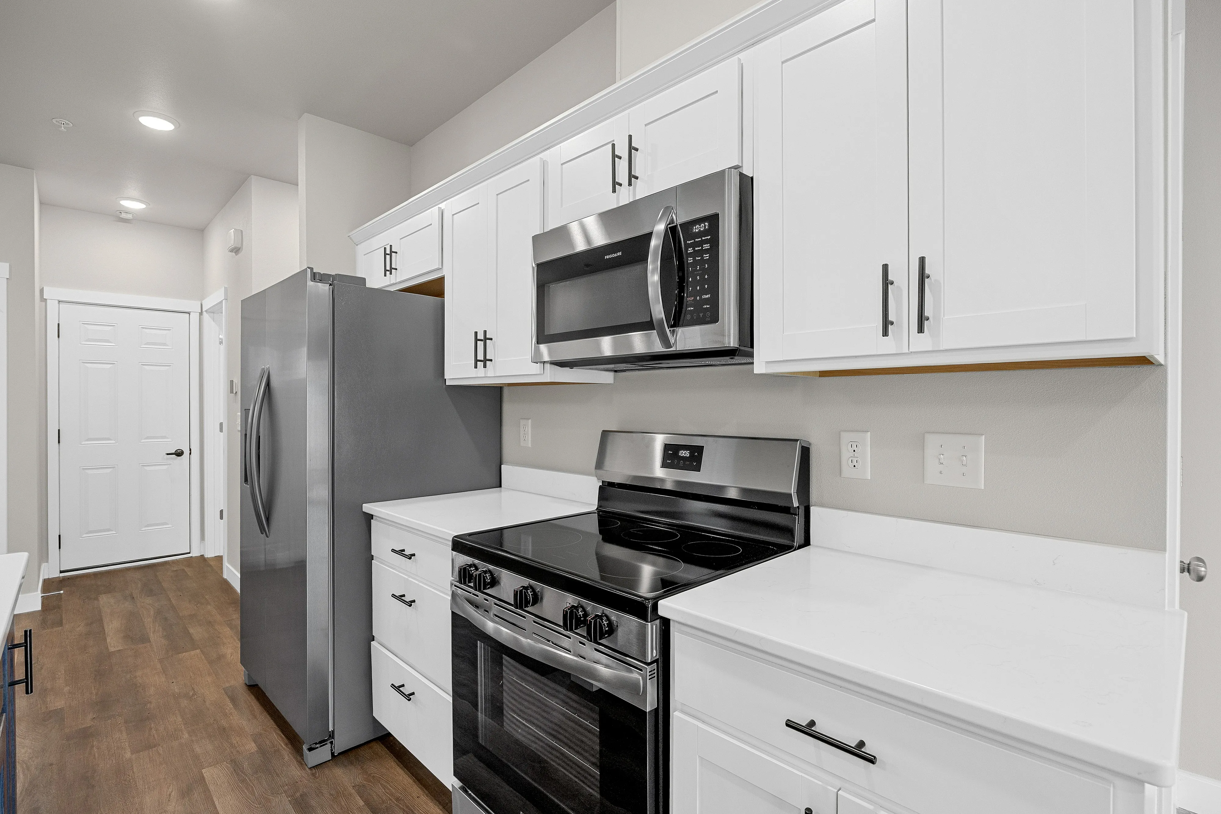 Modern kitchen featuring sleek stainless steel appliances, pristine white cabinetry, and elegant hardwood floors.