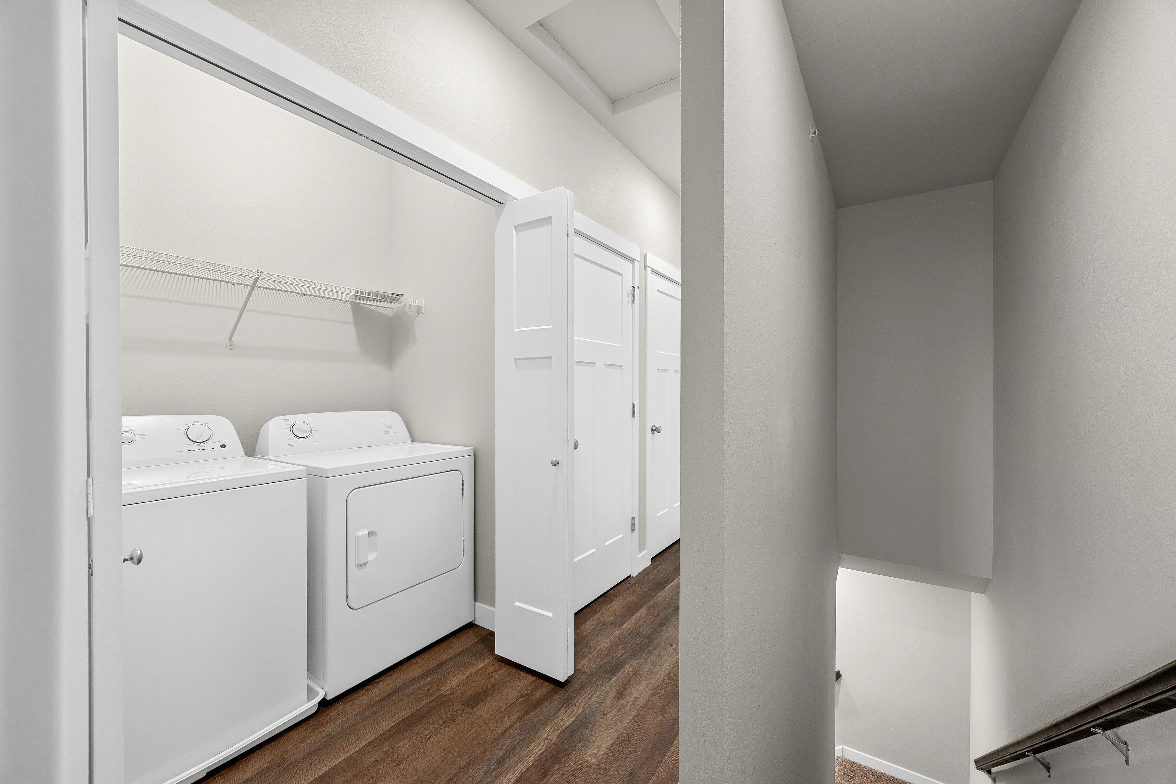 Contemporary laundry area with washer and dryer, showcasing sleek wooden flooring and bright lighting.