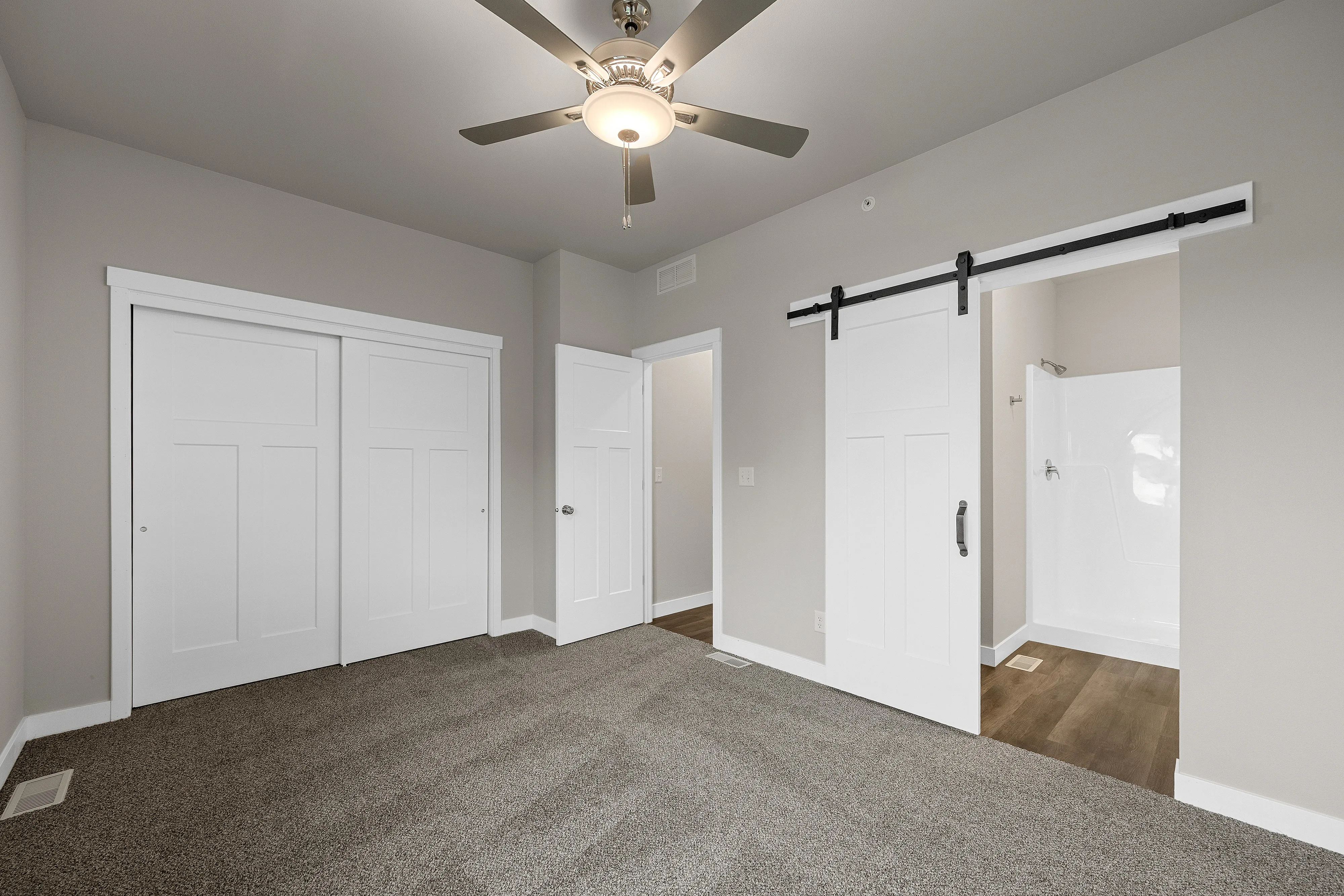 Modern bedroom with plush carpet, sleek ceiling fan, and stylish sliding barn door leading to an en-suite bathroom.