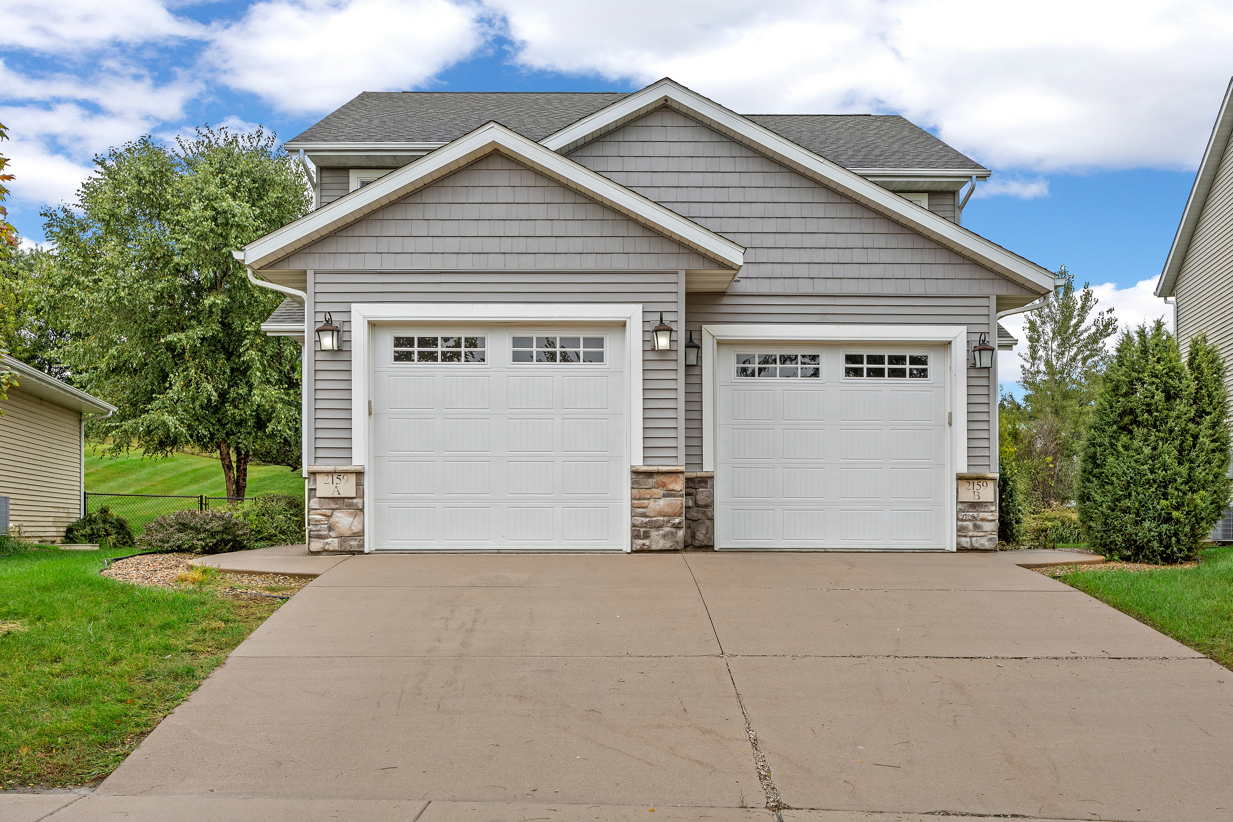Charming suburban home with two-car garage and attractive stone accents, set in a lush, green neighborhood.