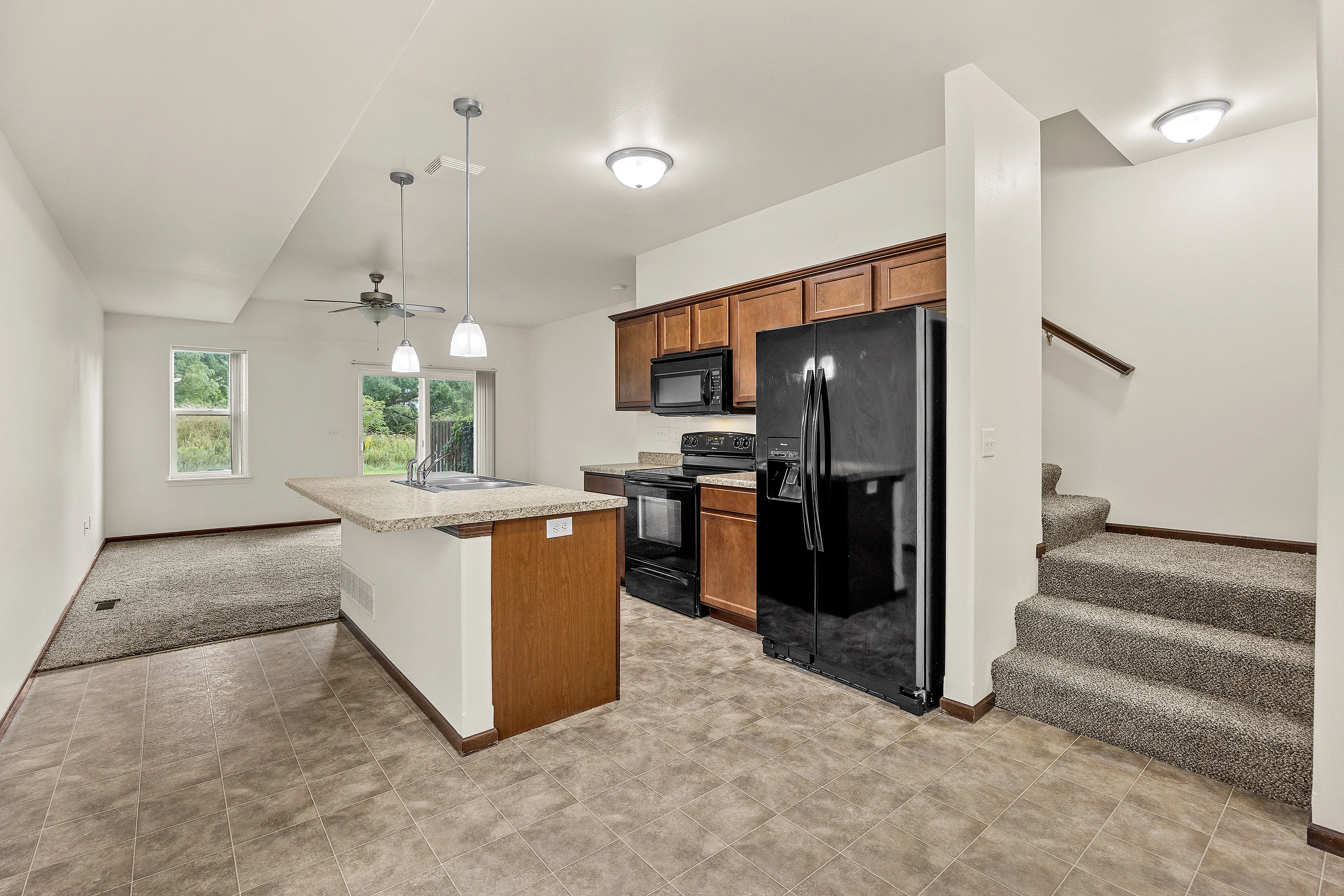 Contemporary open-concept kitchen with sleek black appliances, elegant countertops, and inviting staircase leading to the second floor.