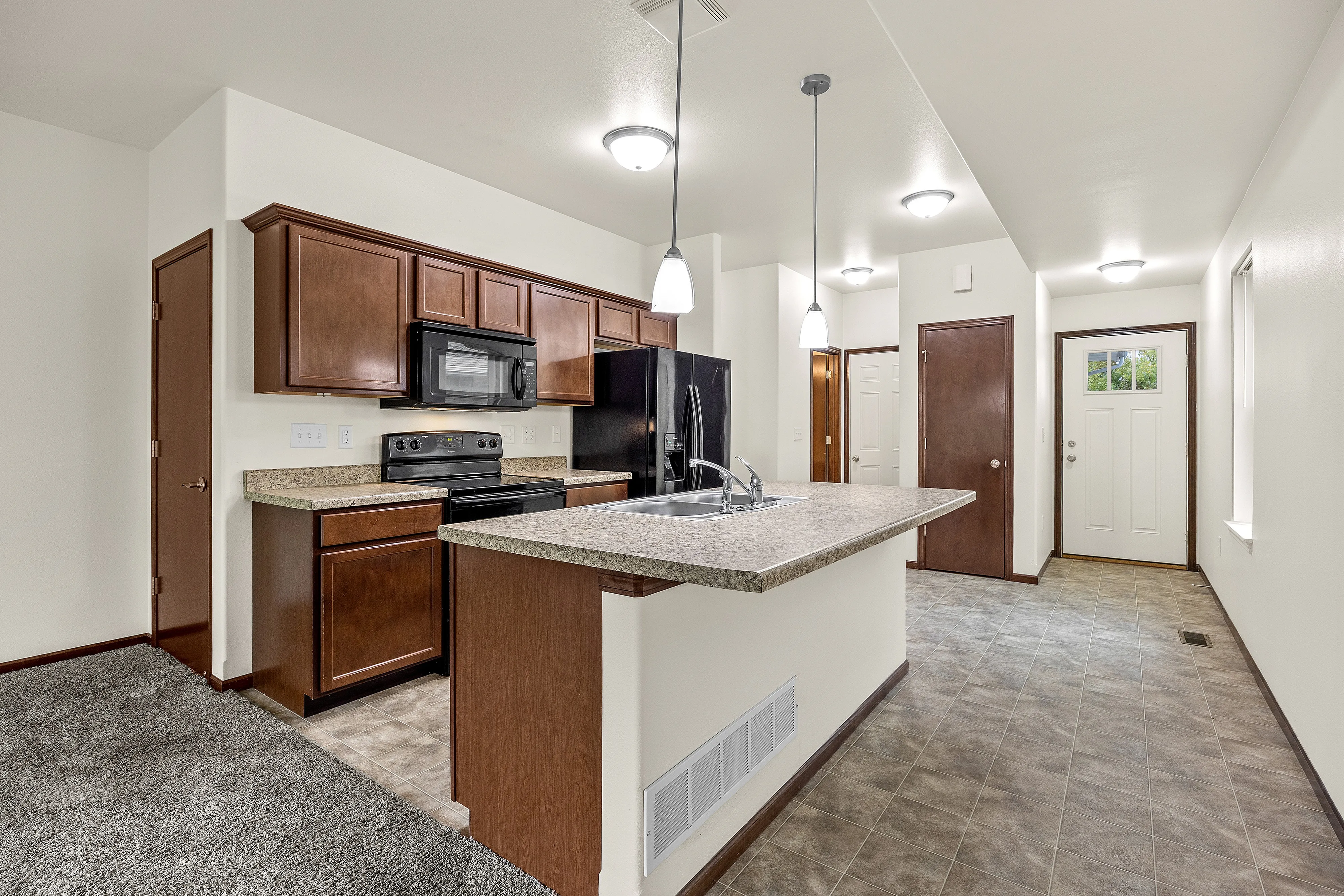 Inviting modern kitchen with rich wood cabinetry, elegant countertops, and a sleek double sink under stylish pendant lighting.