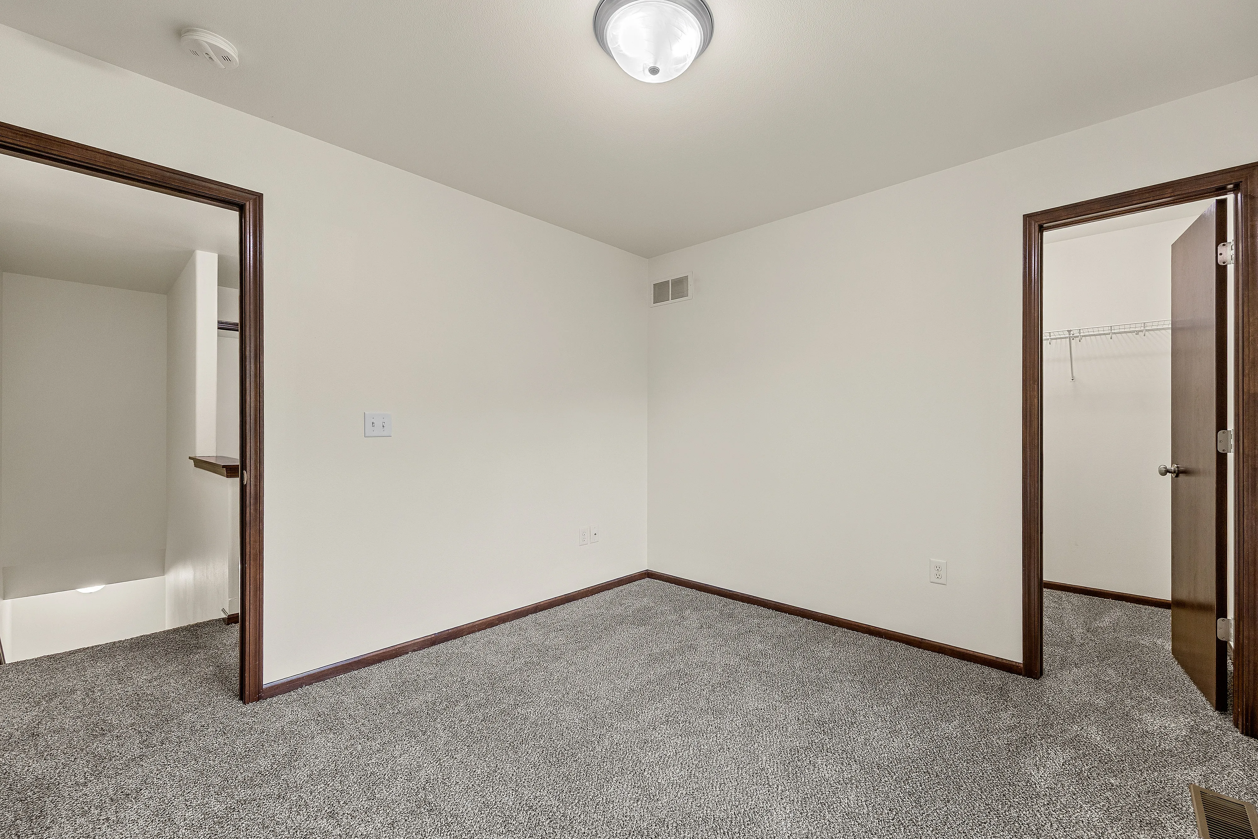 Inviting room with plush carpet, two wooden doorways leading to a closet and a hall, creating a cozy living space.