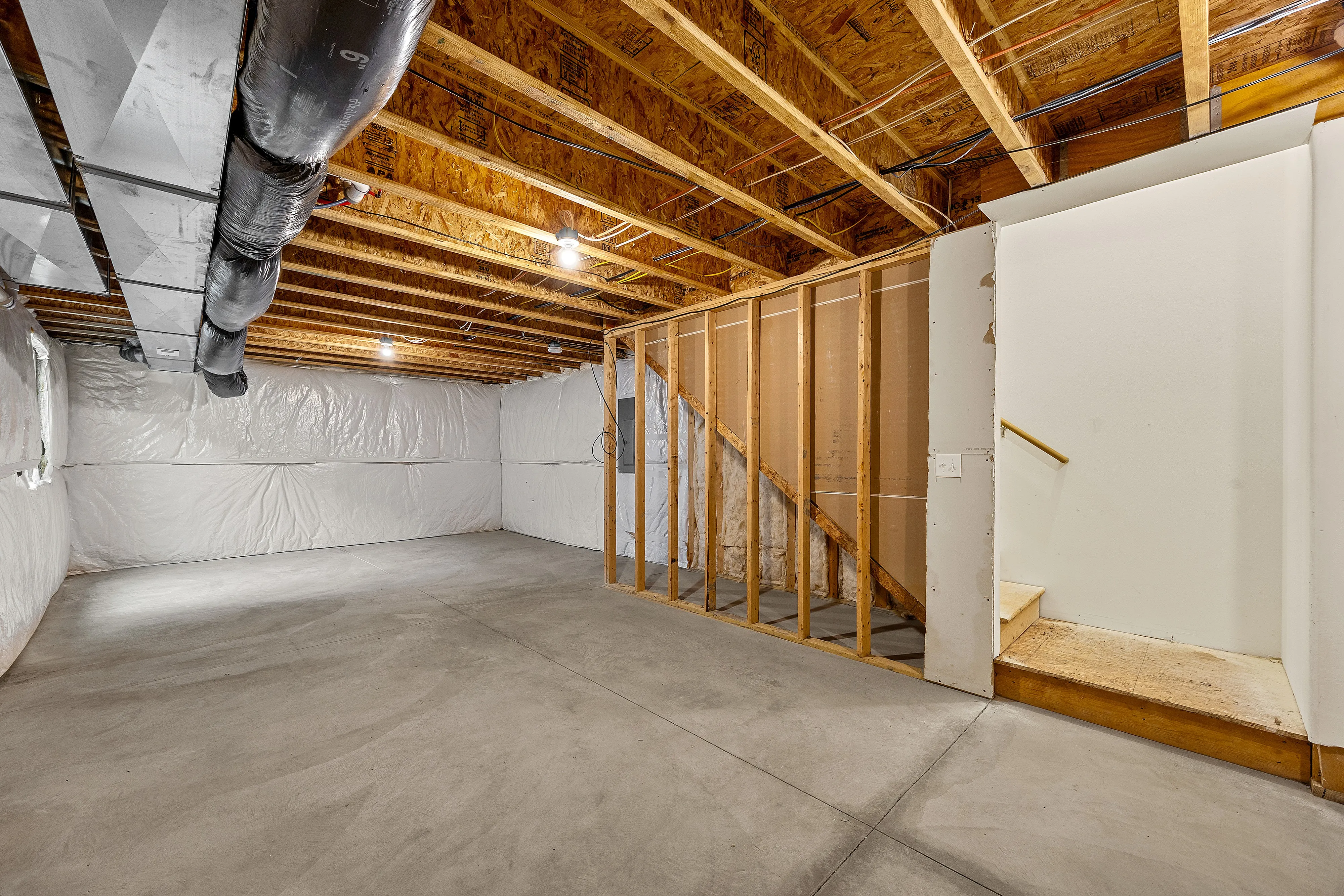 Spacious unfinished basement boasting potential for customization with exposed wooden beams and ductwork.