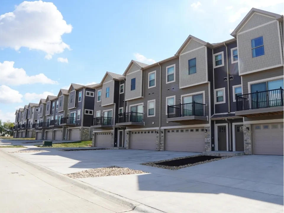 Charming row of modern townhouses with private balconies, spacious driveways, and scenic blue sky backdrop.