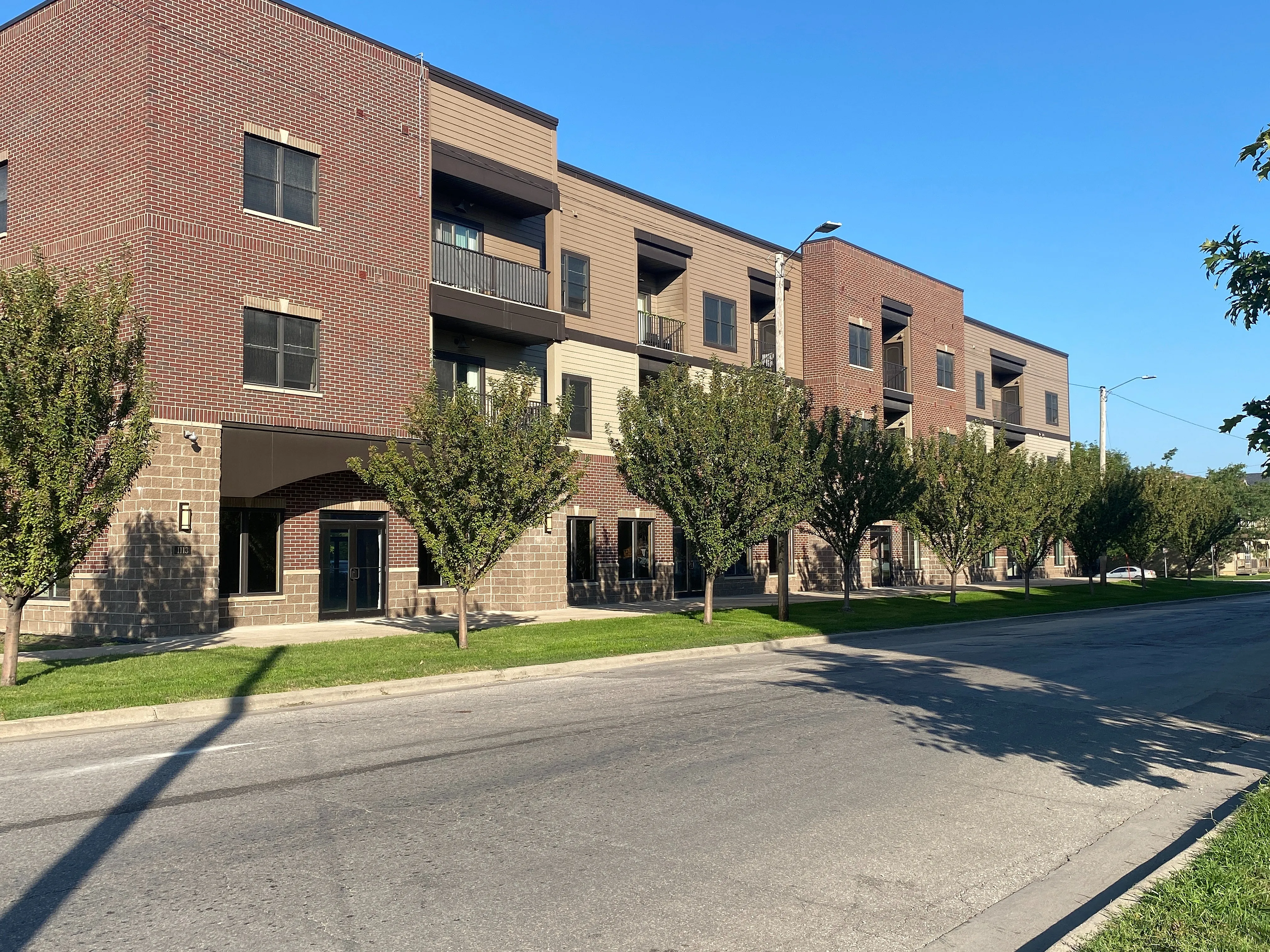 Modern apartment building with a stylish brick facade, lush greenery, and spacious balconies, offering a blend of urban convenience and serene living.